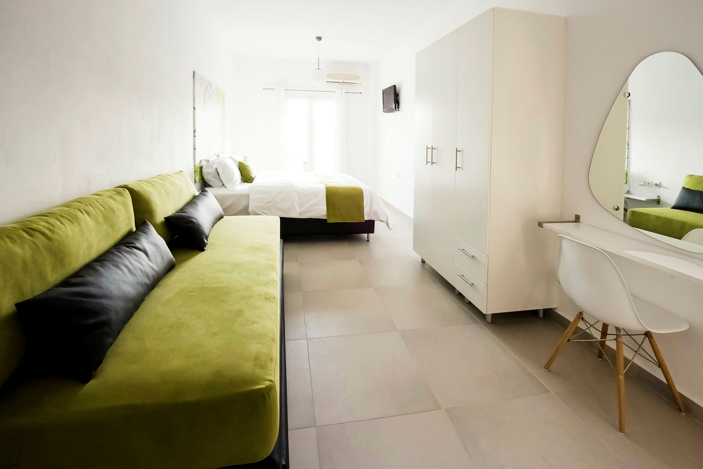 Modernt möblerat hotellrum med grön soffa, säng, garderob och skrivbord med spegel. (AI-genererad text)