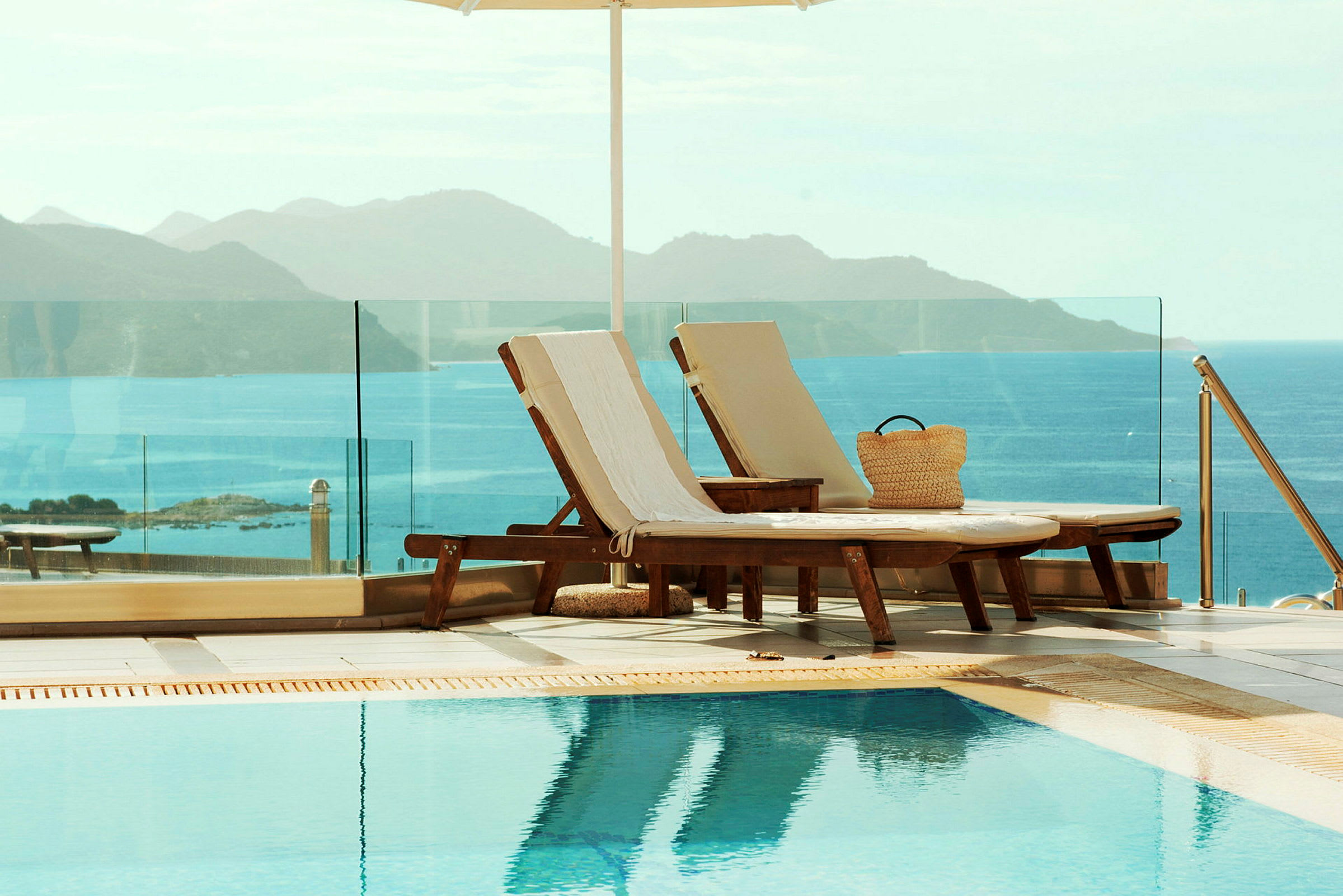 Två solstolar vid en pool med utsikt över havet och bergen. (AI-genererad text)