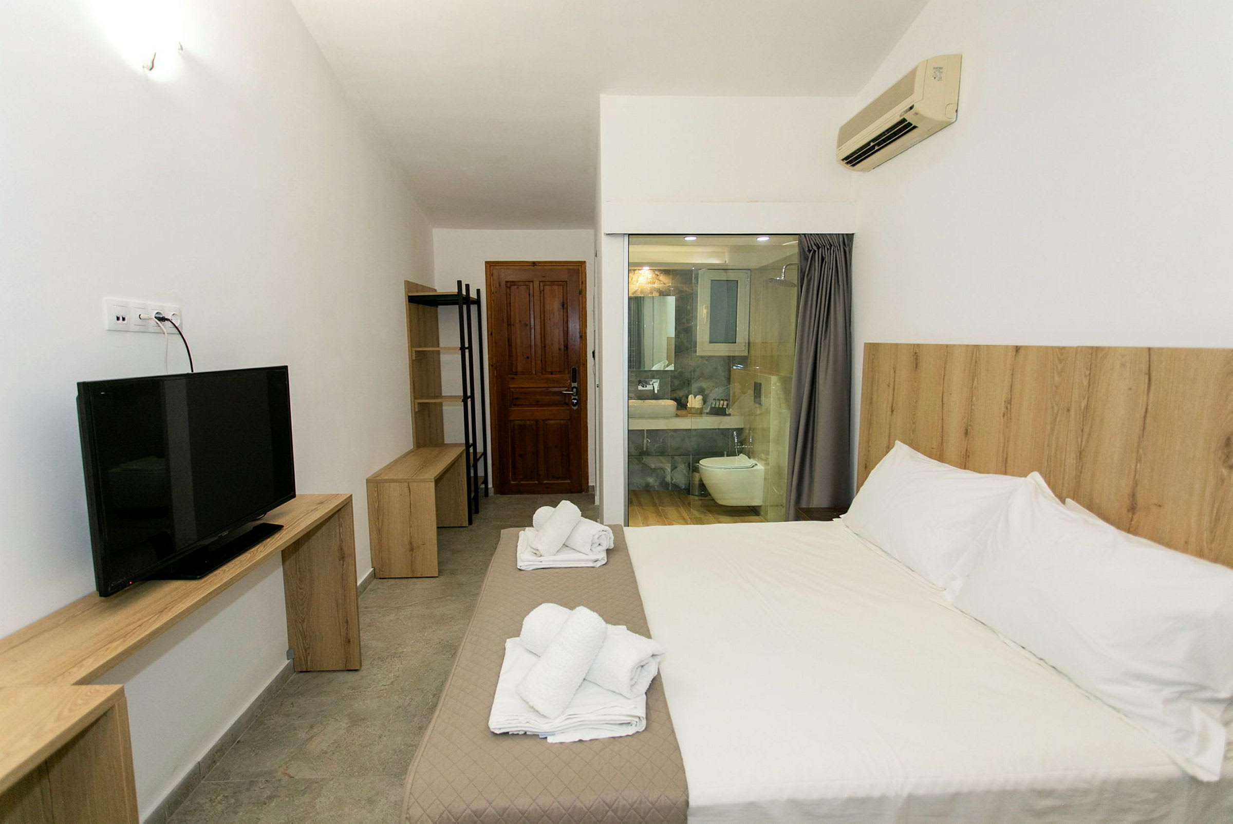 Ett hotellrum med en stor säng, TV, trädetaljer och ett öppet badrum. (AI-genererad text)