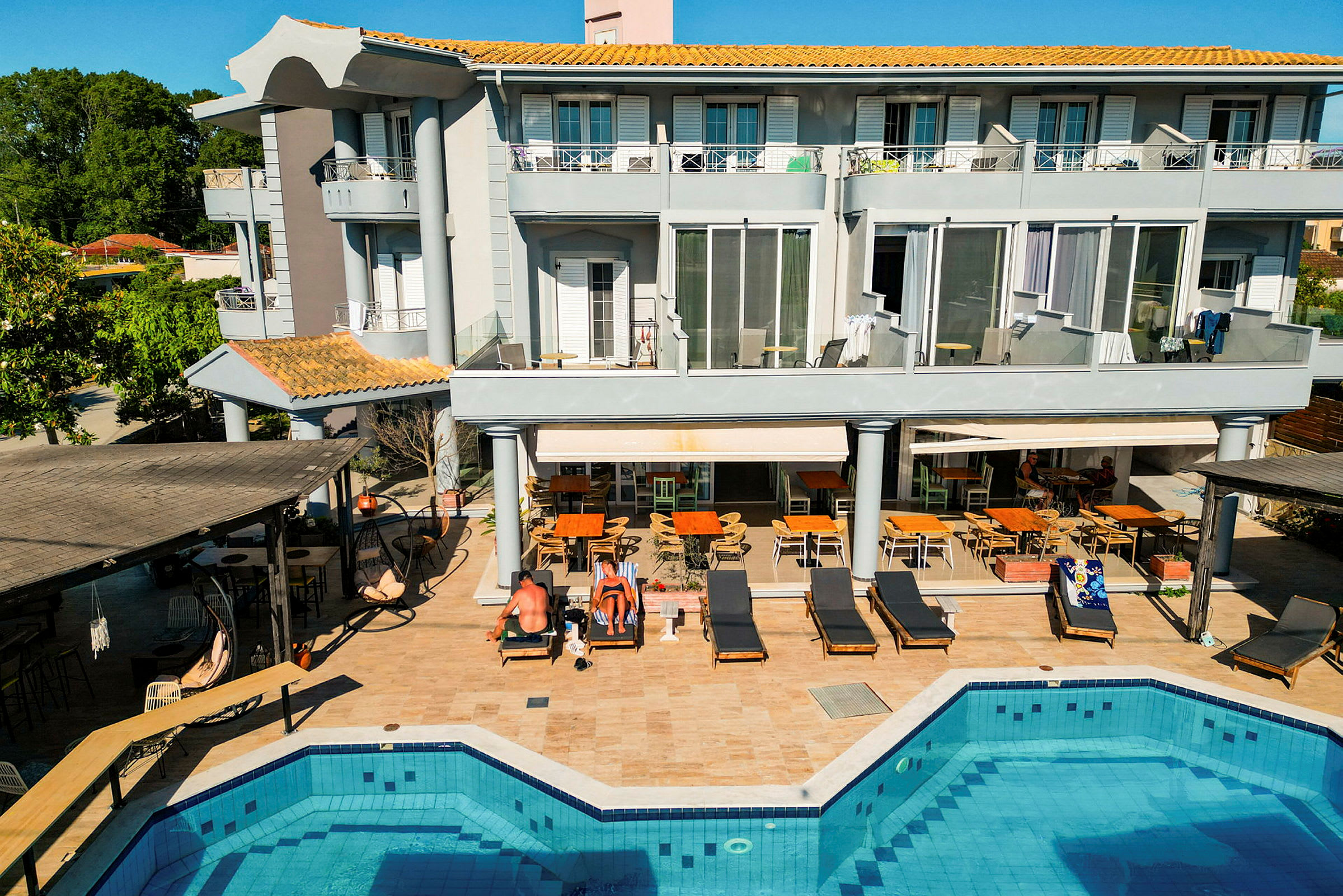 Ett trevåningshotell vid en pool med omgivande solstolar och sittplatser. (AI-genererad text)