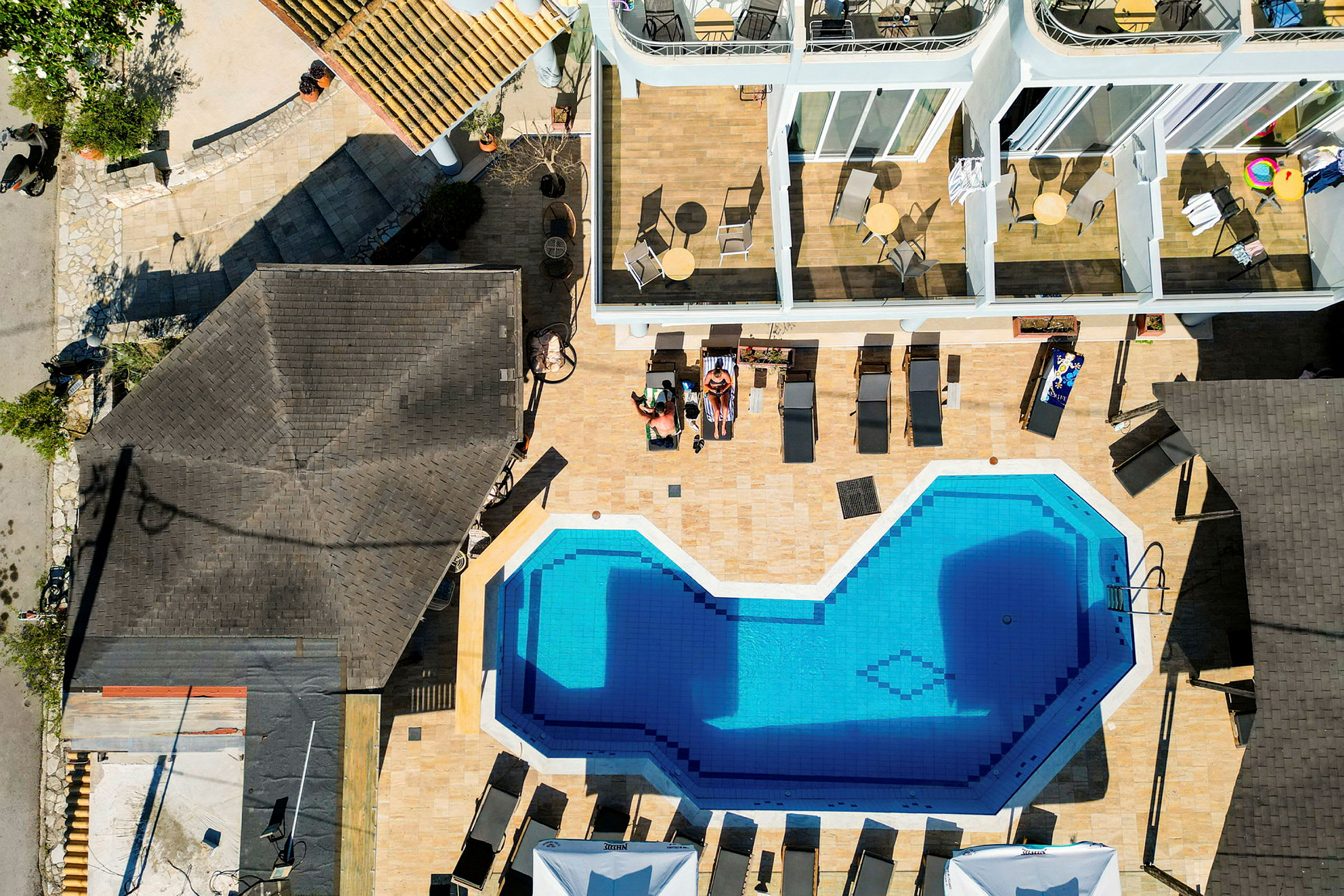 Drönarbild av en swimmingpool omgiven av solstolar och byggnader med terrasser. (AI-genererad text)