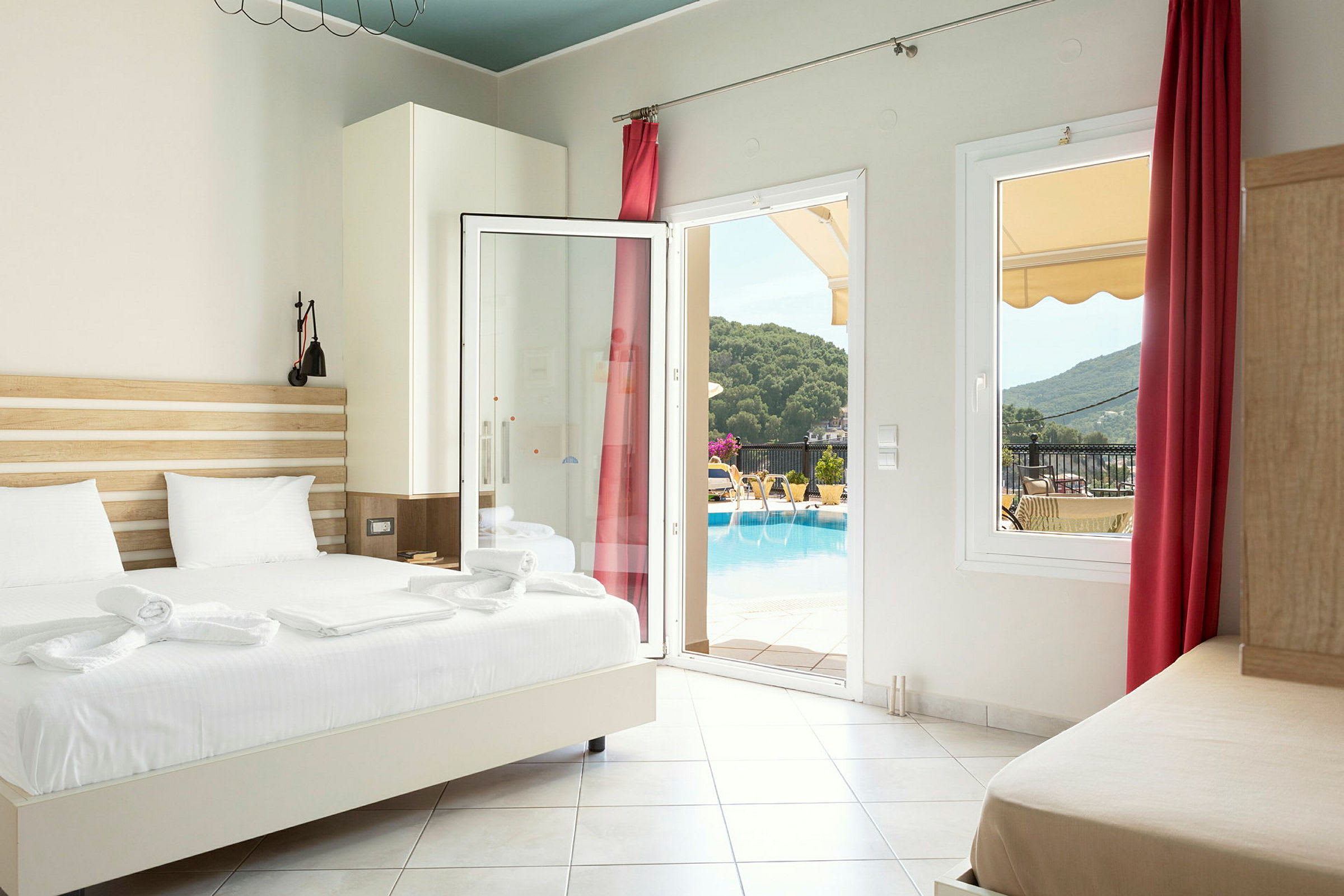 Hotellrum med säng, öppet glasparti och utsikt mot poolområde och omgivande grönska. (AI-genererad text)