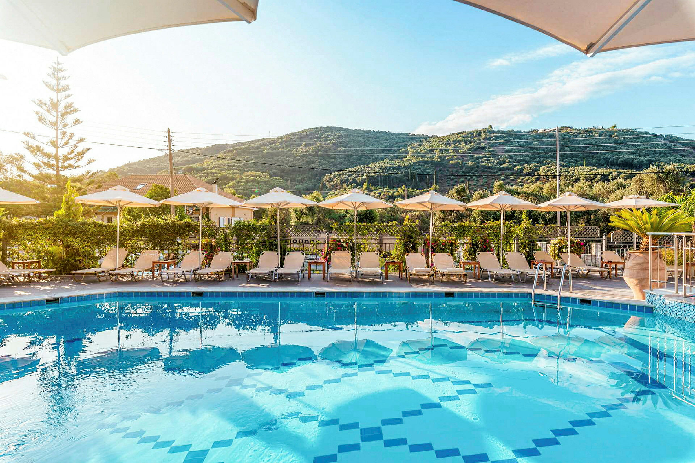 Pool med solstolar och parasoller framför en grön bergsutsikt. (AI-genererad text)
