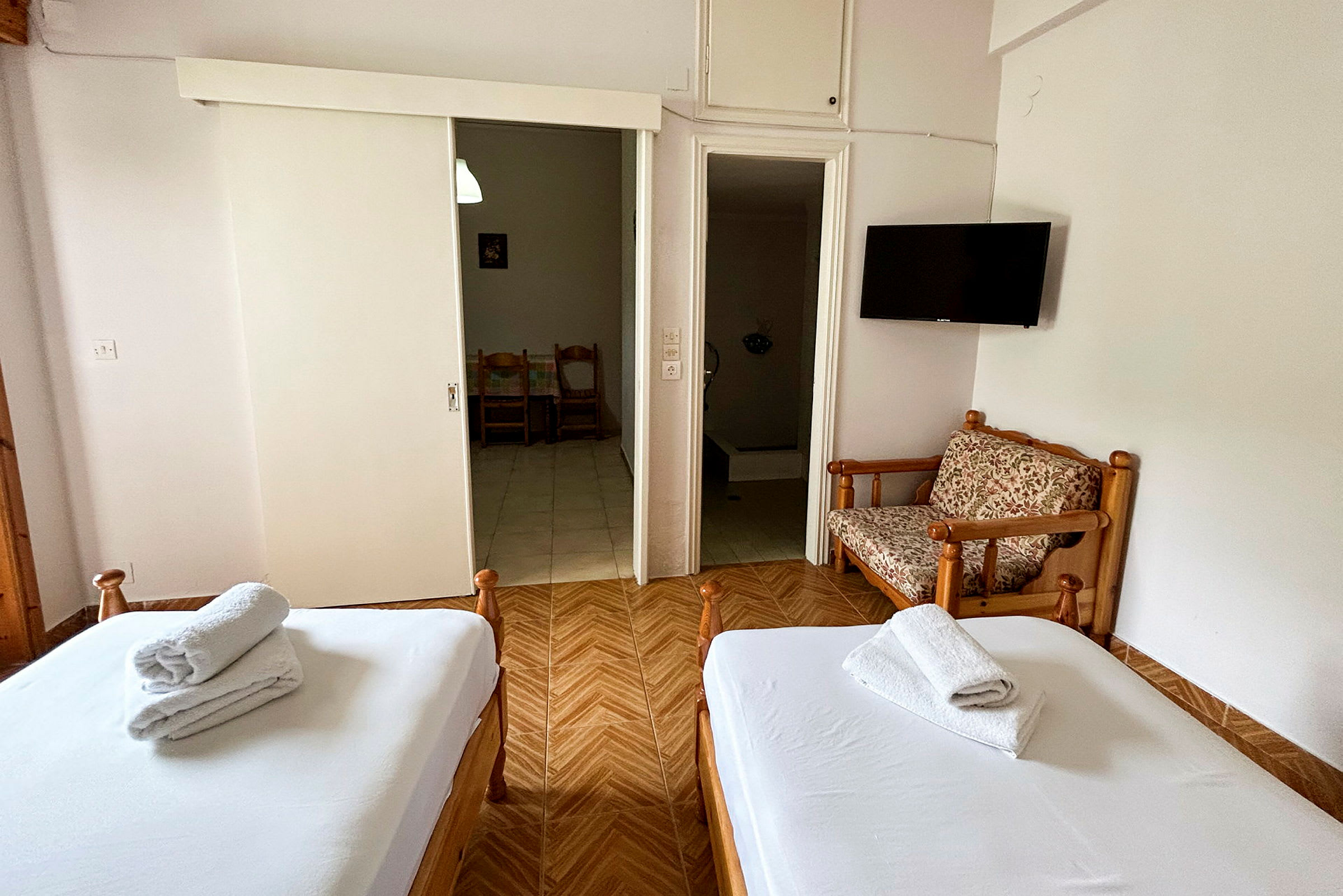 Ett hotellrum med två bäddar, en stängd garderob, en liten sittmöbel och en TV på väggen. (AI-genererad text)