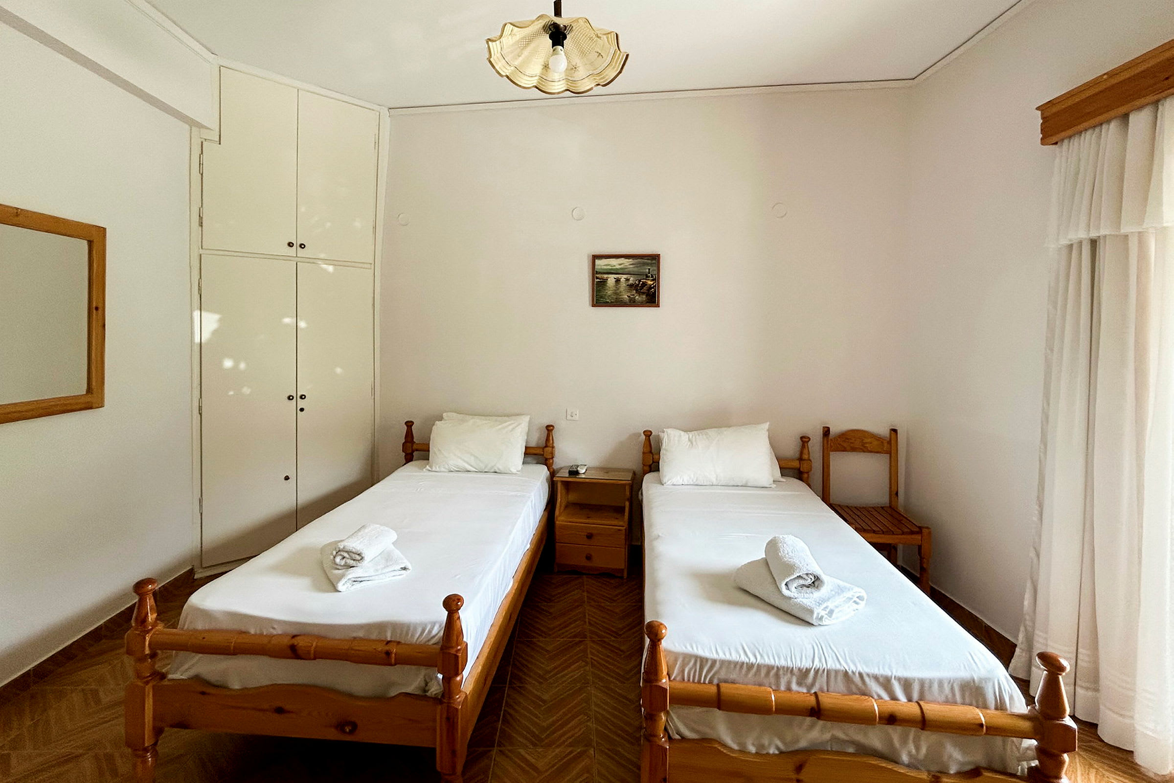 Bild av ett hotellrum med två enkelsängar och vita sängkläder, belägna vid en ljus vägg med ett litet väggskåp. (AI-genererad text)