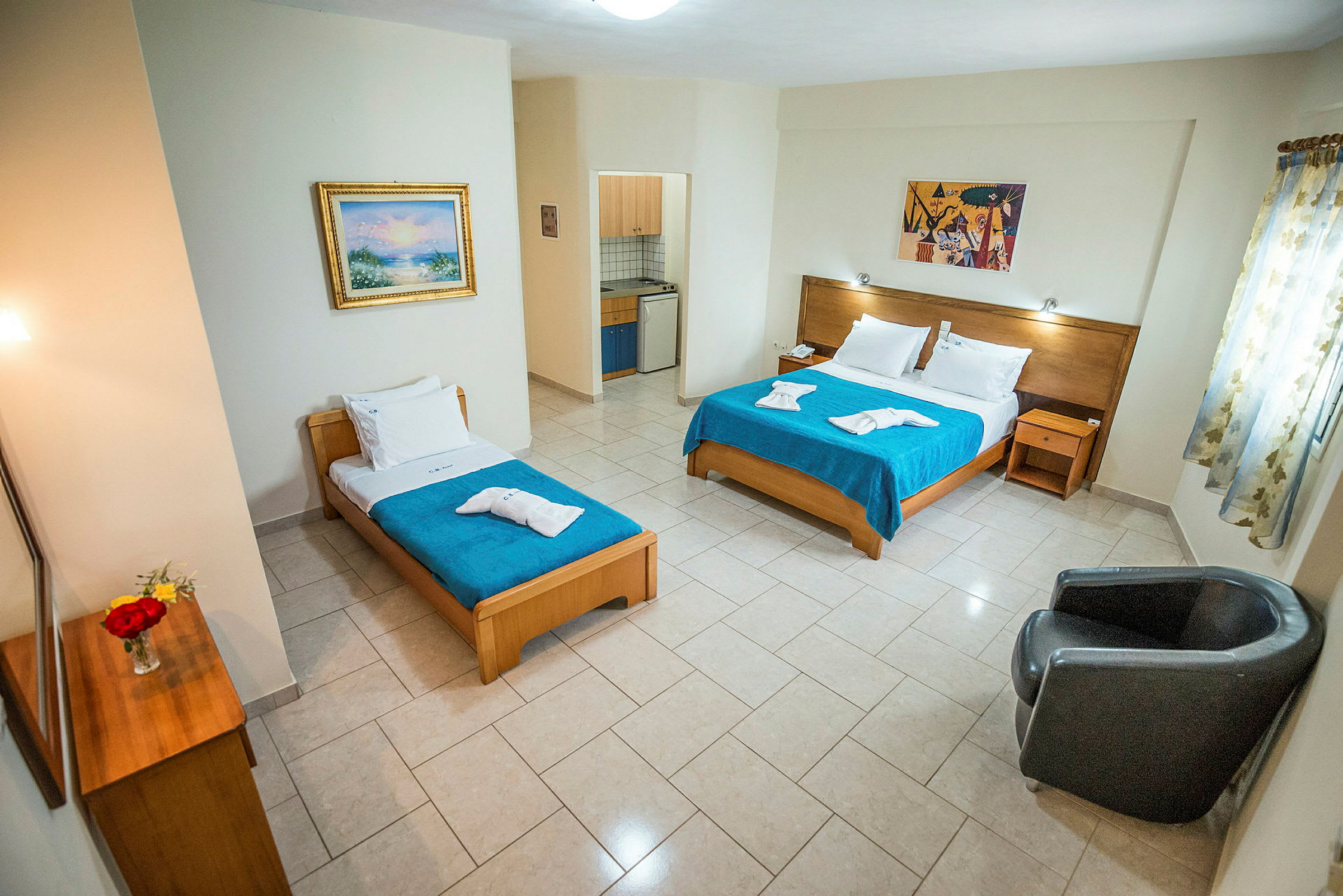 Hotellrum med dubbelsäng och enkelsäng, liten köksdel samt sittplats. (AI-genererad text)