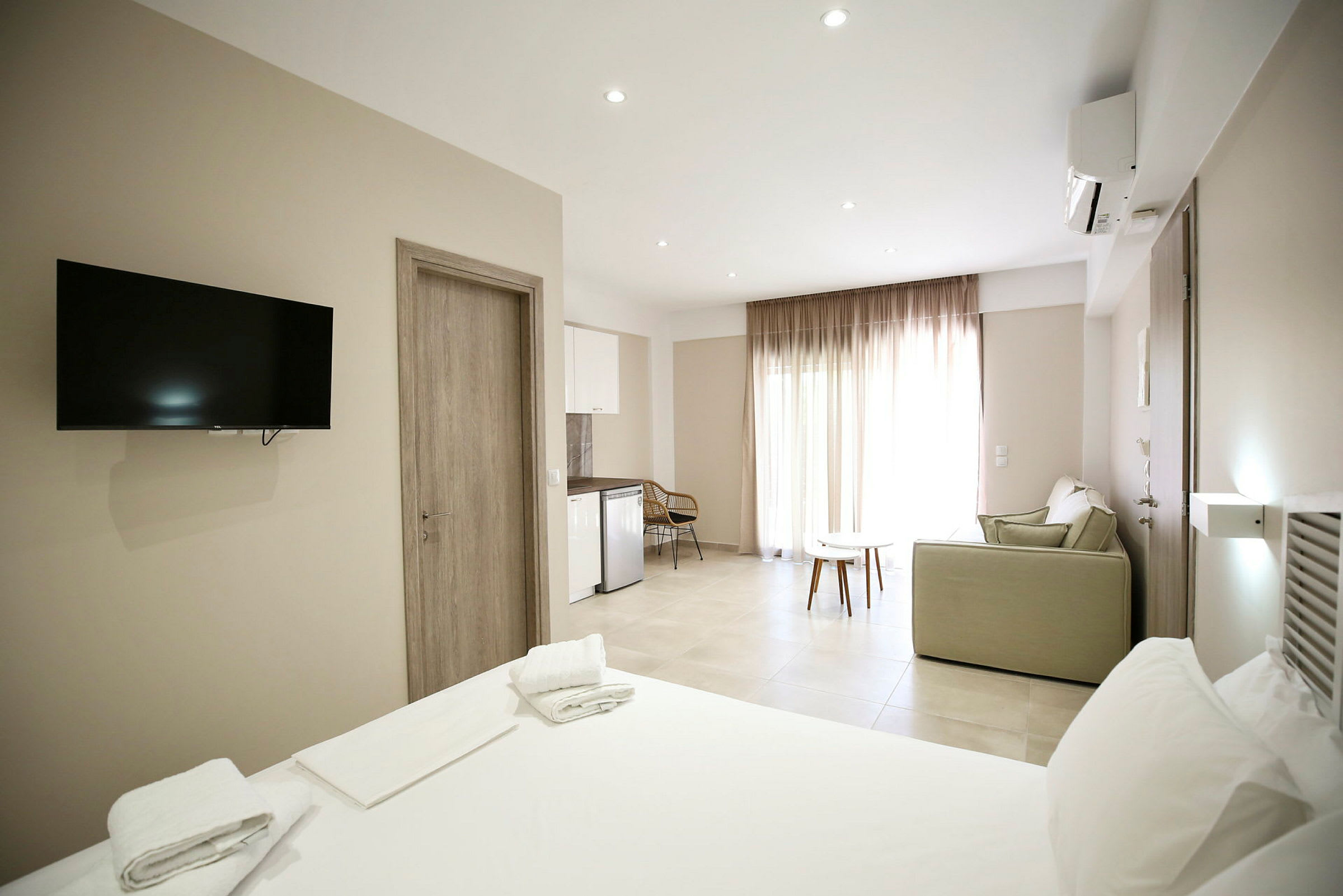 Ett ljus och luftigt hotellrum med en säng, tv, soffa och ett litet kök. (AI-genererad text)