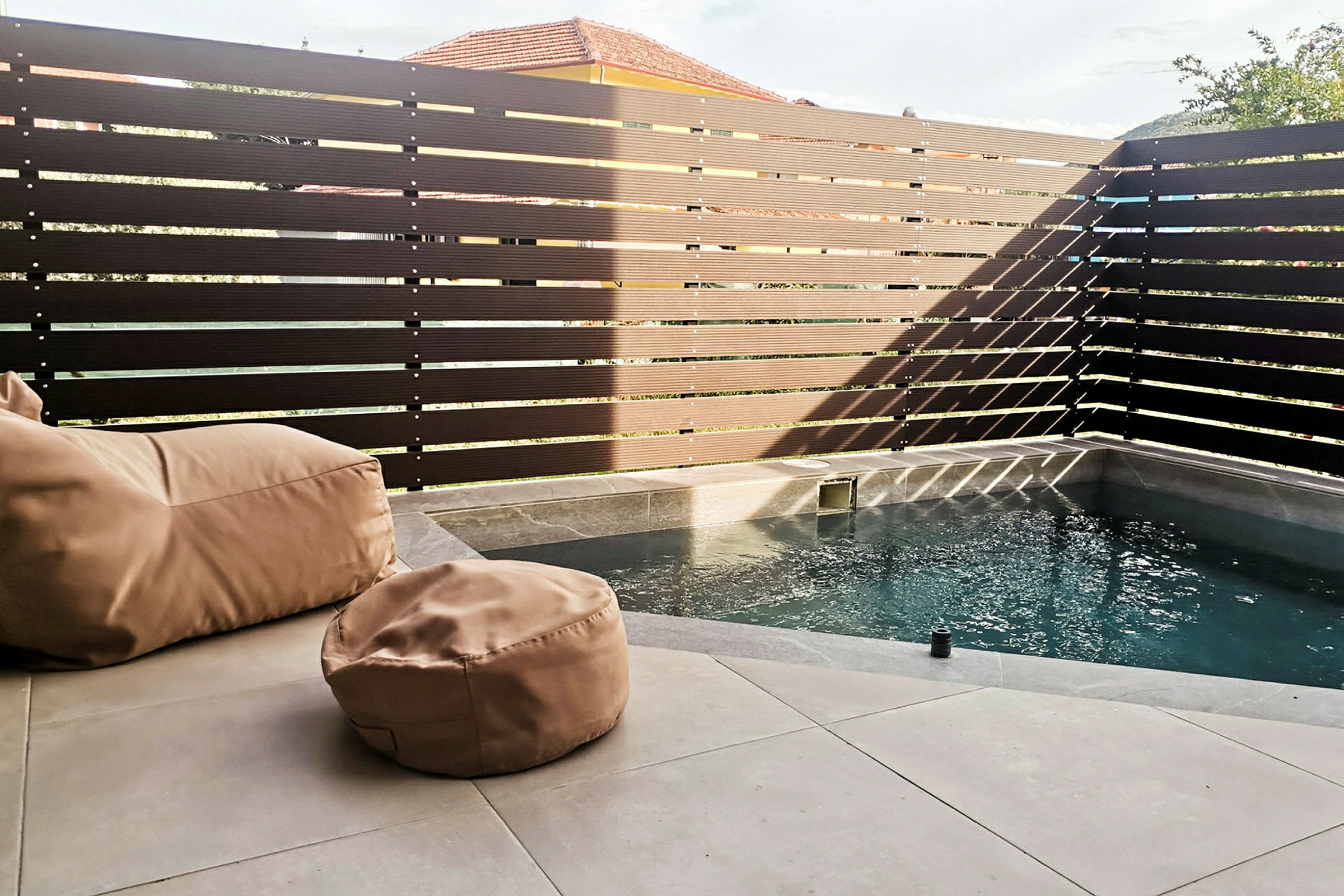 Liten pool med beige sittsäckar på en stenyta, omgiven av ett högt, mörkt staket. (AI-genererad text)