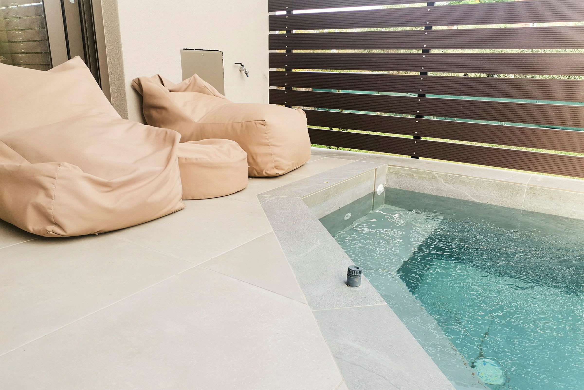 Två beige sittsäckar bredvid en liten pool på en terrass. (AI-genererad text)