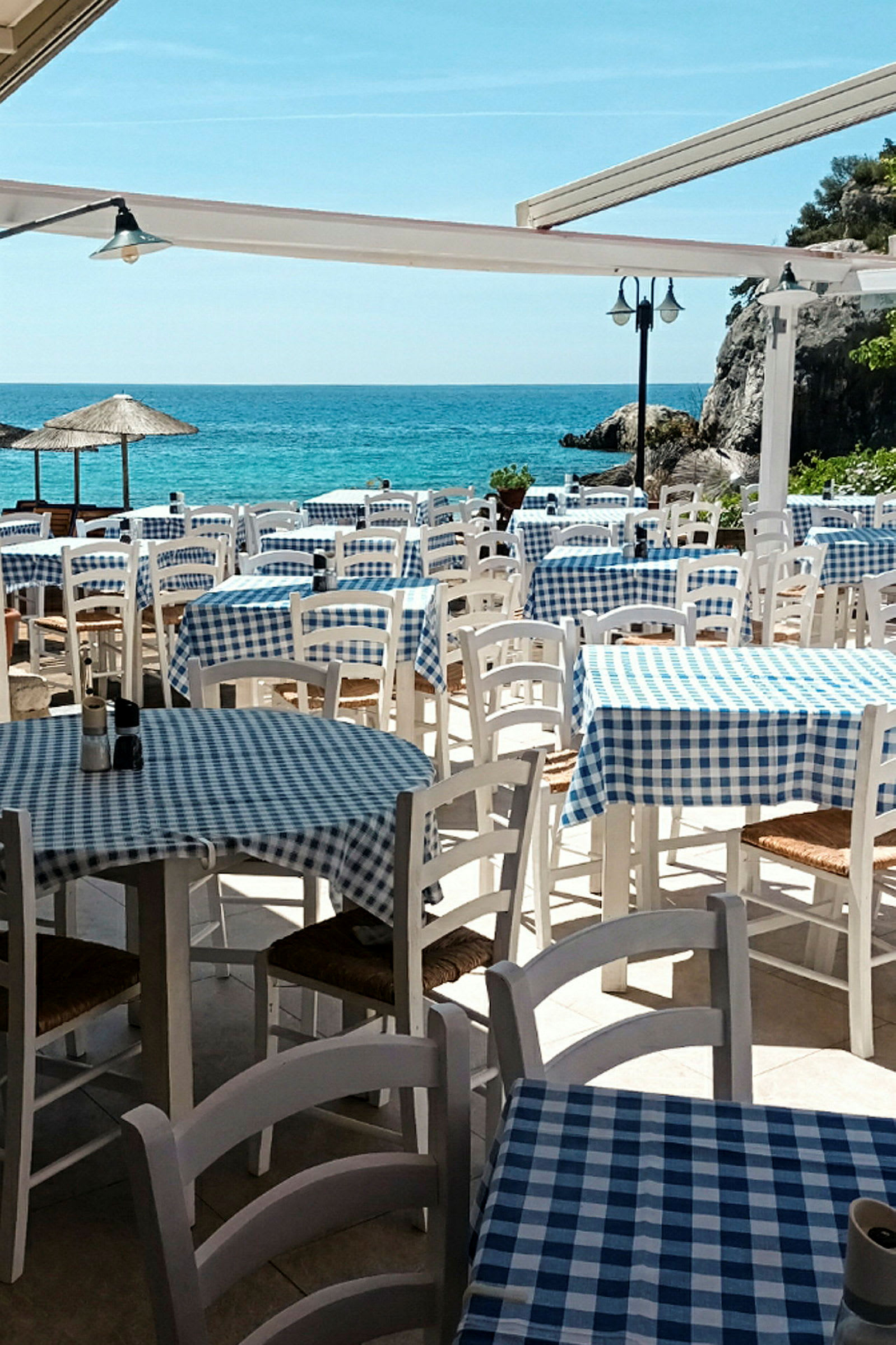 Restaurang vid havet med dukade bord och stolar utomhus. (AI-genererad text)