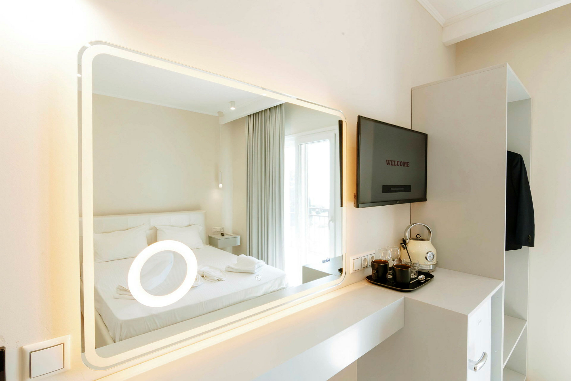 Spegel som reflekterar ett hotellrum med en säng och en TV-apparat, med en hylla innehållande kaffetillbehör. (AI-genererad text)