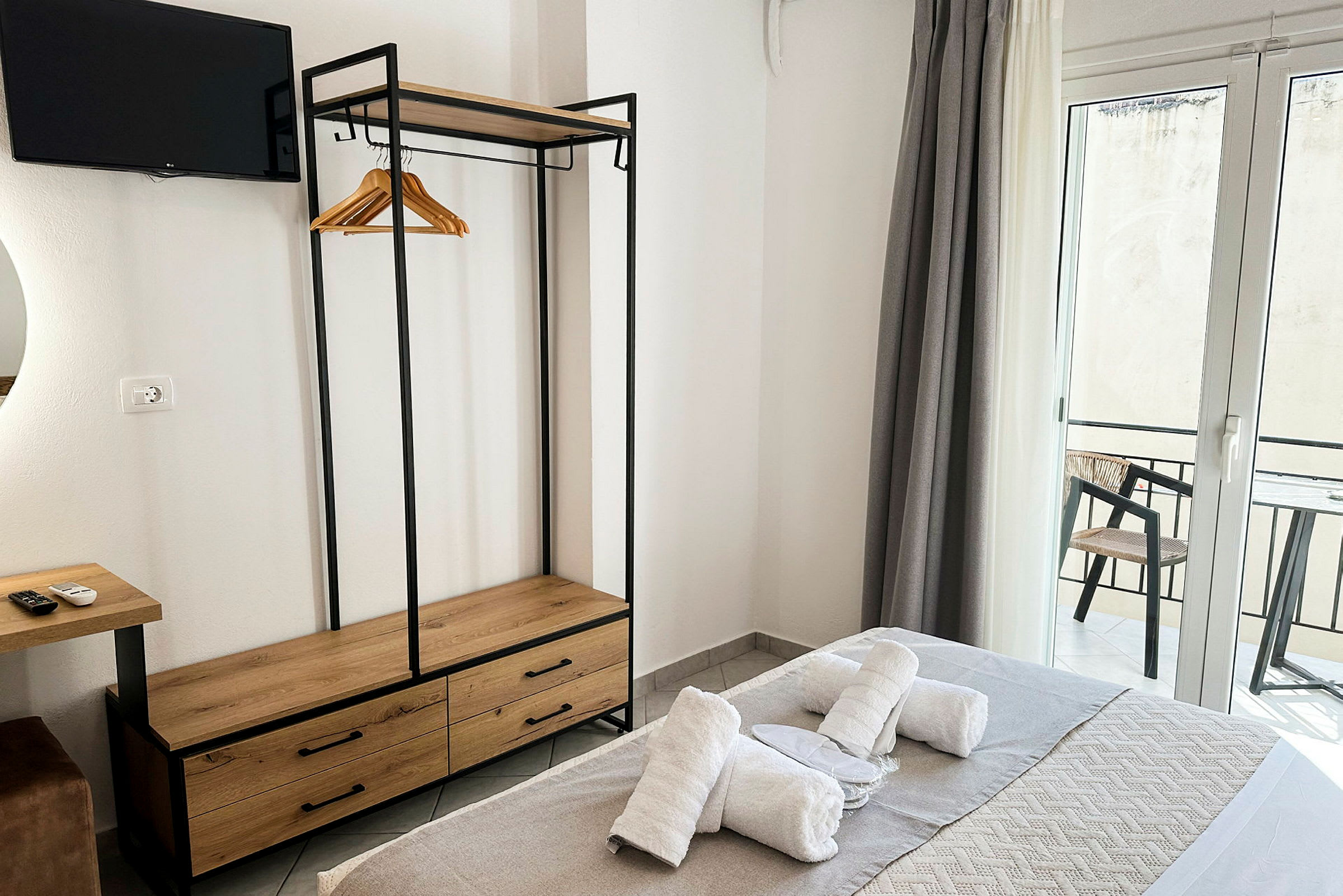 Ett hotellrum med säng utrustad med handdukar, garderob med klädgalgar, TV och balkong med utsikt. (AI-genererad text)
