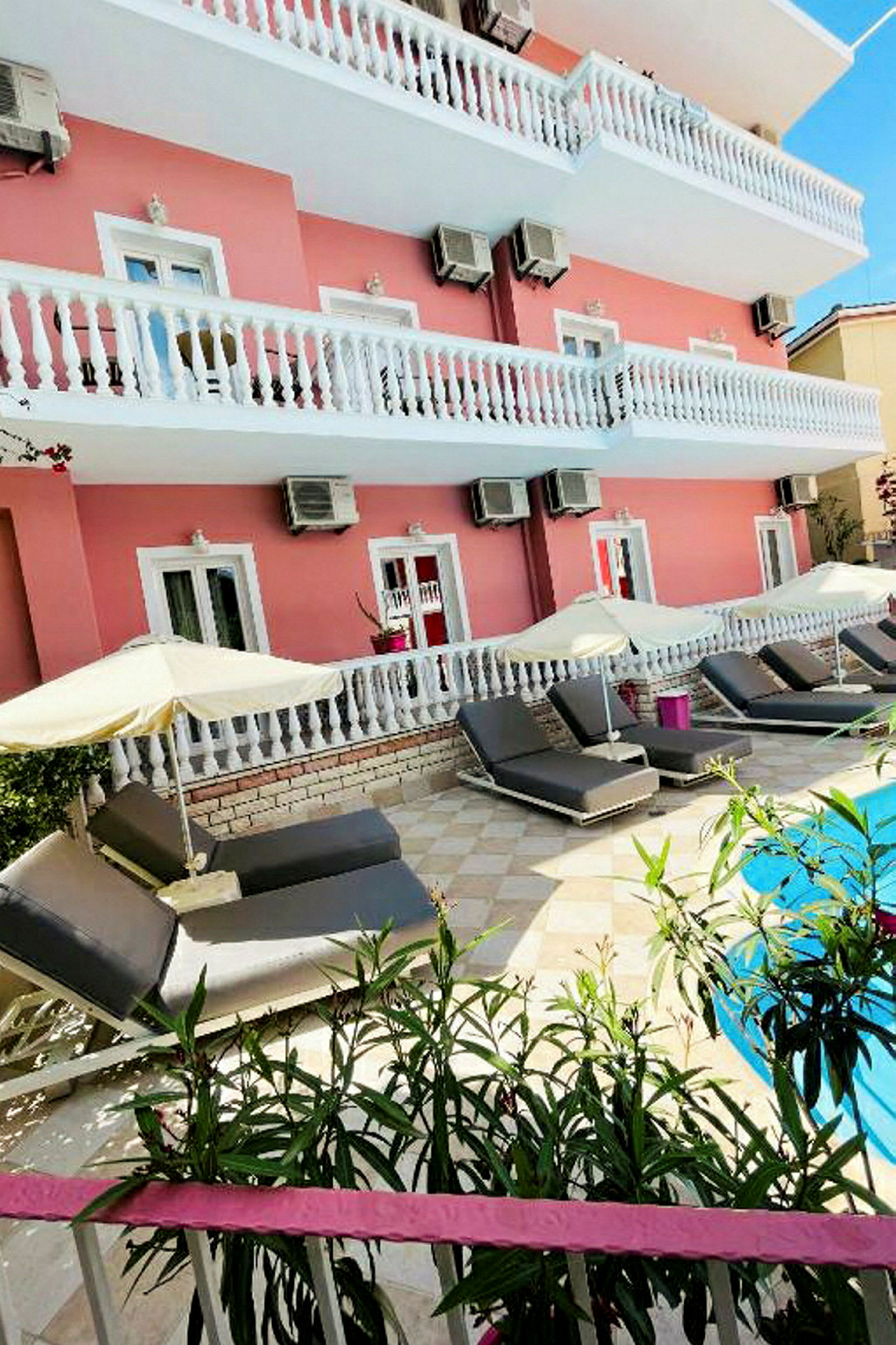 Hotellbyggnad med rosa fasad, balkonger och solstolar vid en pool. (AI-genererad text)