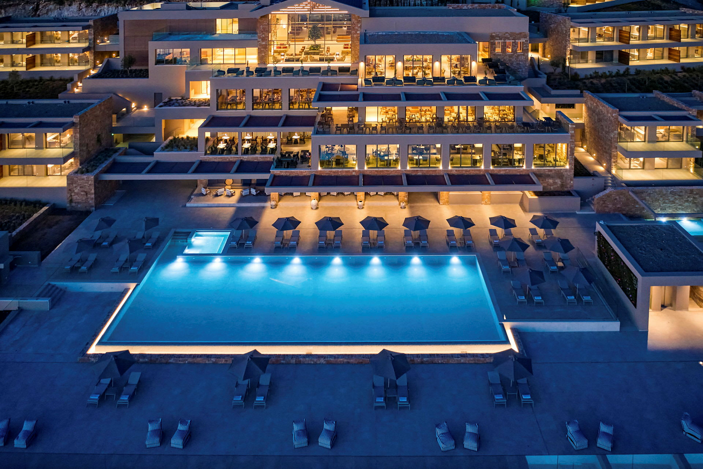 Vy över ett hotell med en pool, utomhusområden och belysning på kvällen. (AI-genererad text)