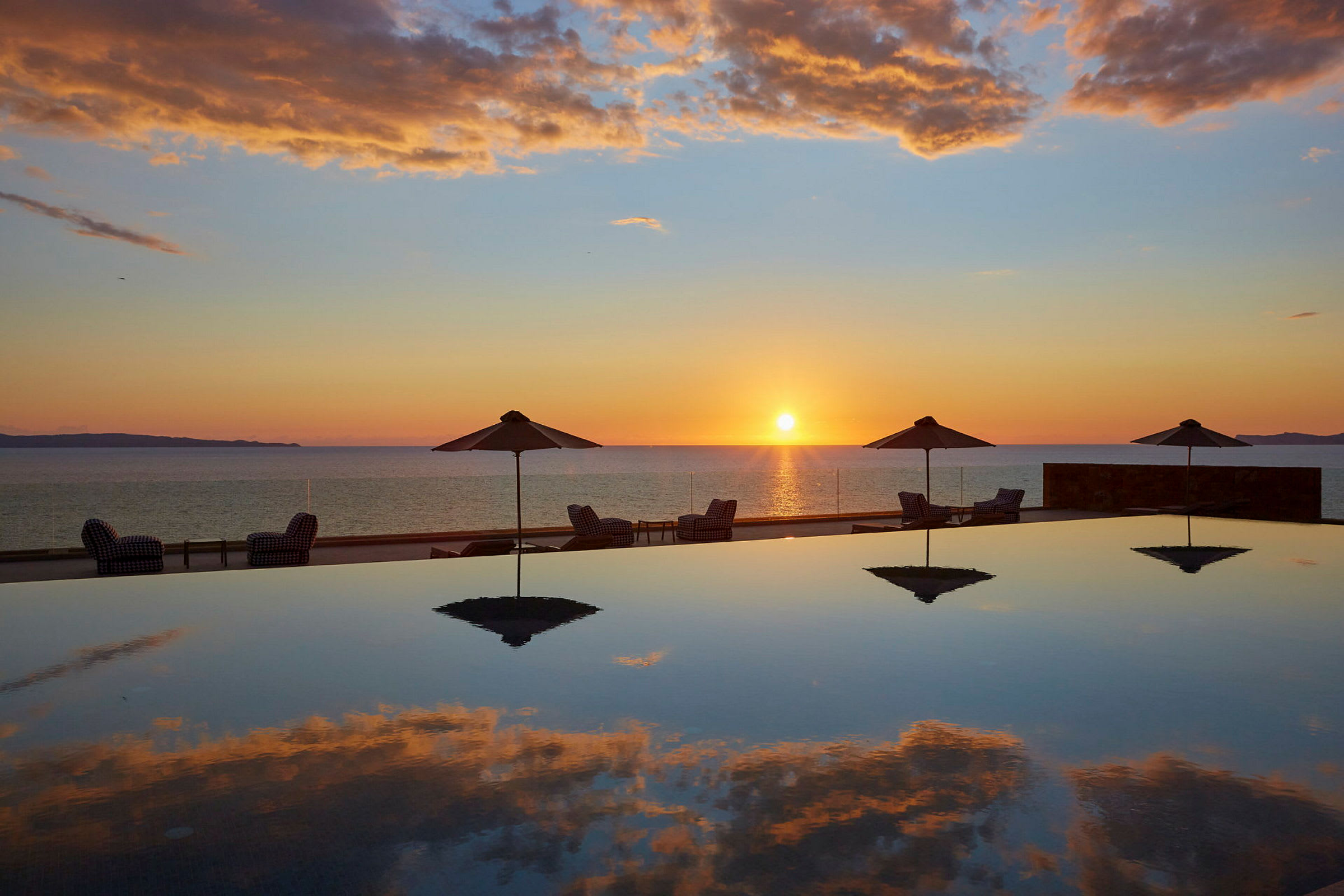 Solnedgång över havet med parasoller och solstolar vid en pool. (AI-genererad text)