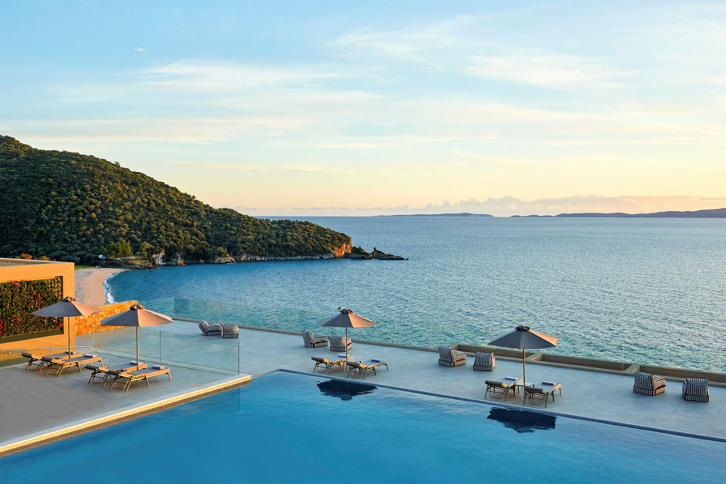 En infinitypool med solstolar och parasoller, med utsikt över havet och en grönskande kust. (AI-genererad text)