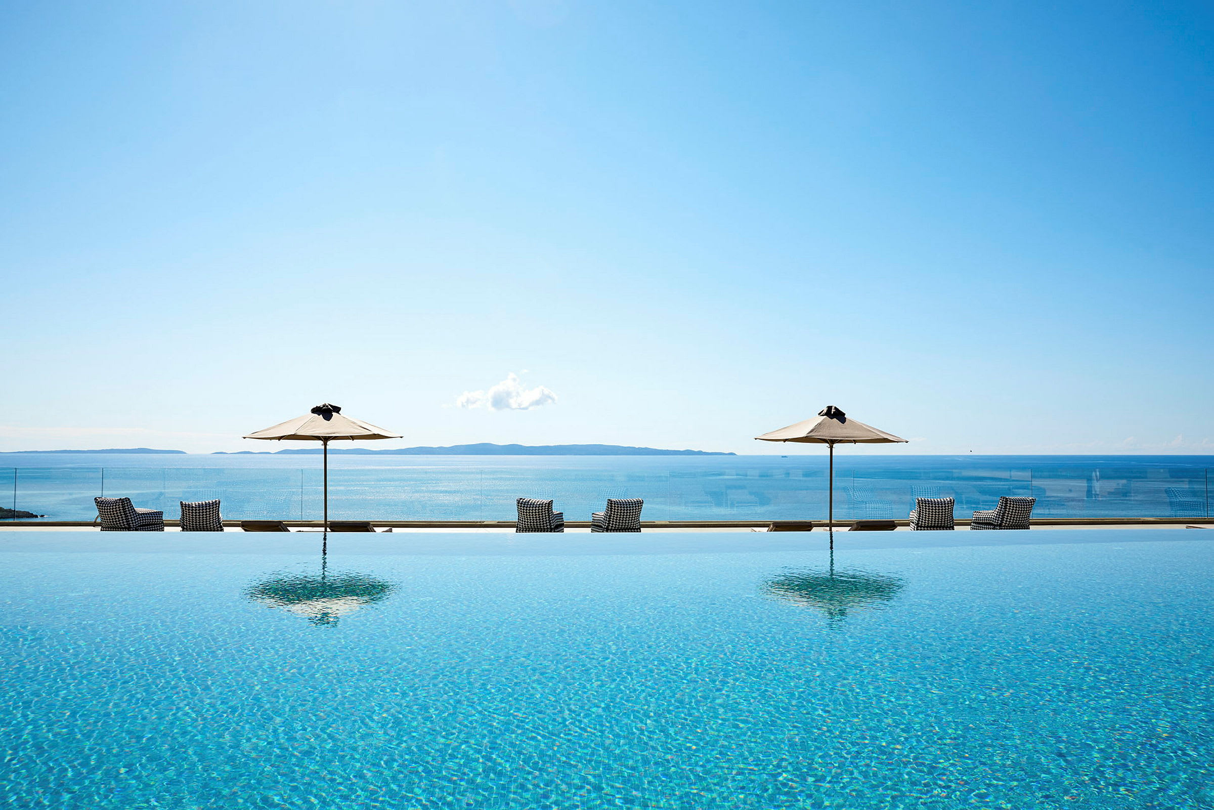 Infinitypool med utsikt över havet, omgiven av solstolar och parasoller. (AI-genererad text)
