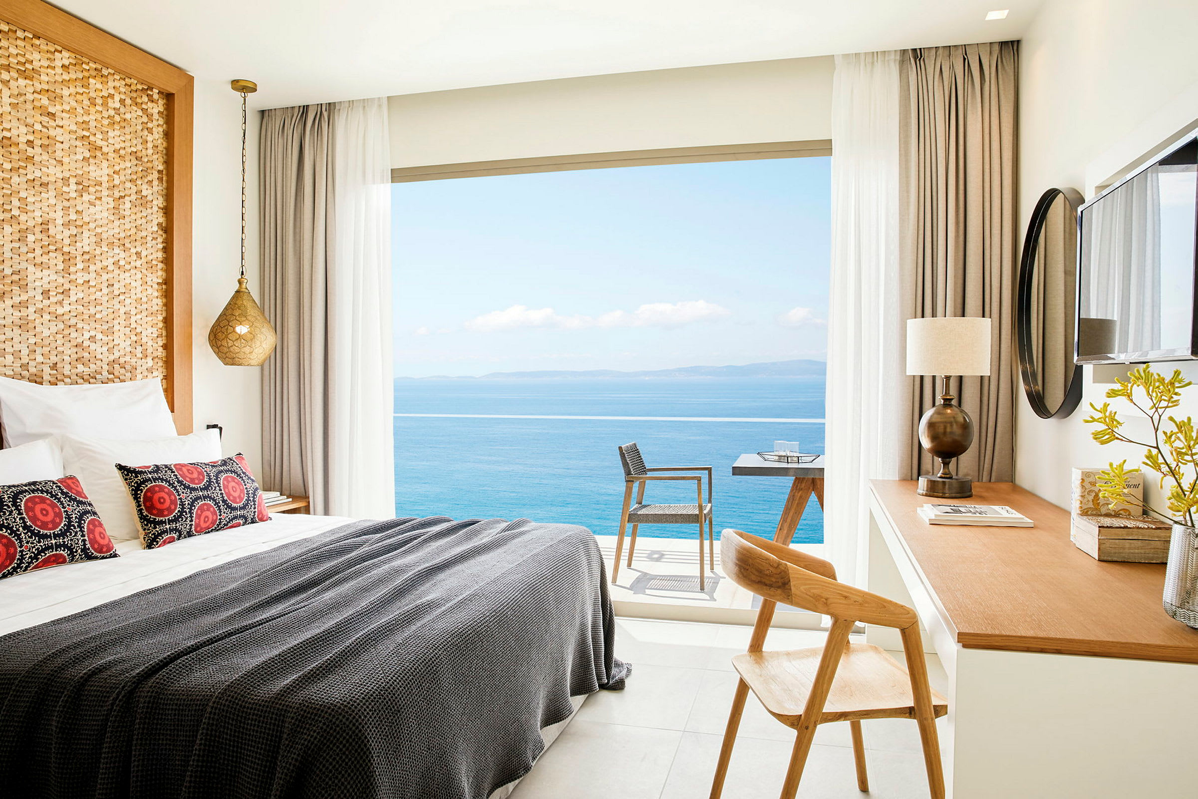 Ett hotellrum med en bäddad säng, skrivbord och utsikt över havet genom fönstret. (AI-genererad text)