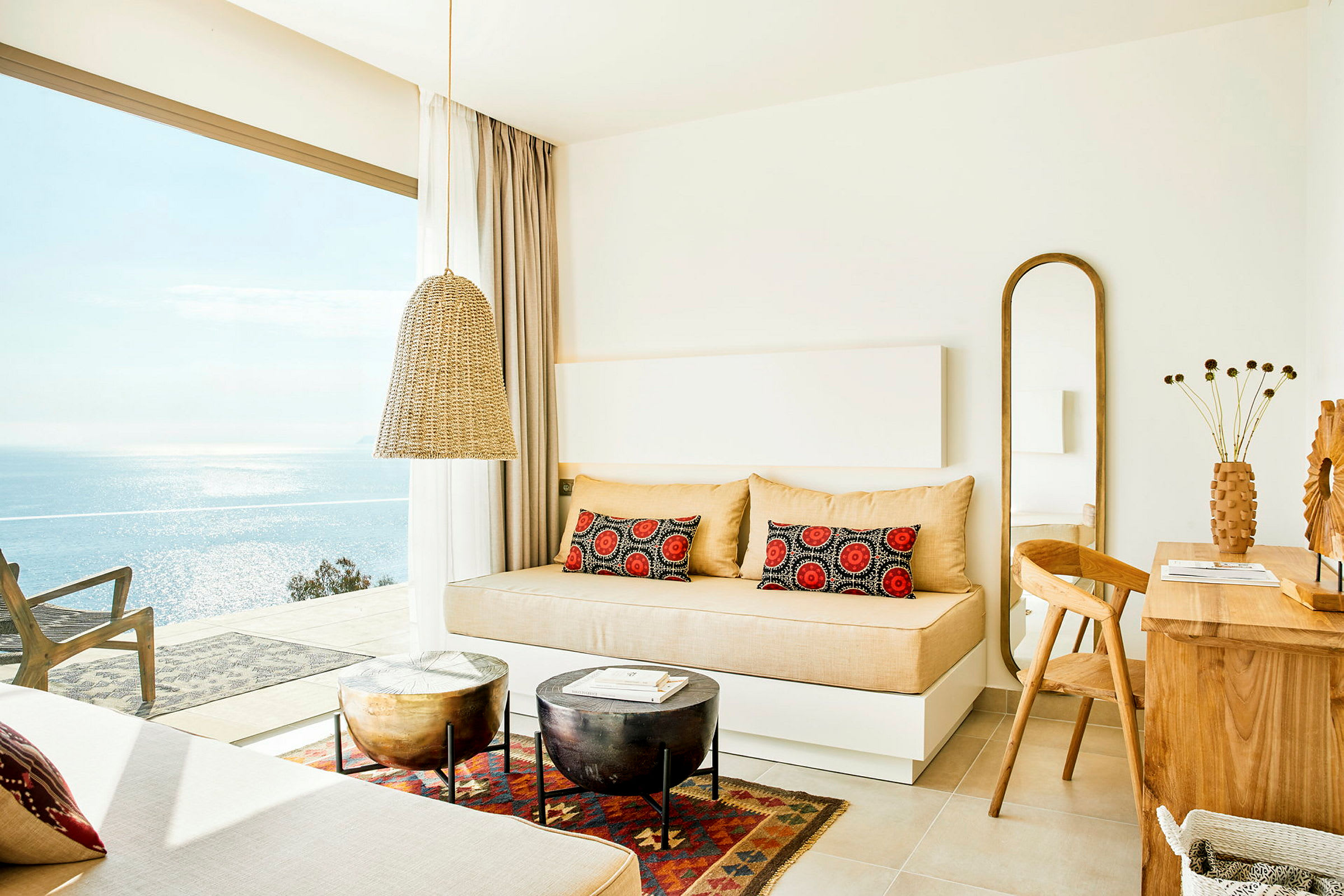Ljus hotellrum med bäddsoffa, träbord och havsutsikt genom stora fönster. (AI-genererad text)