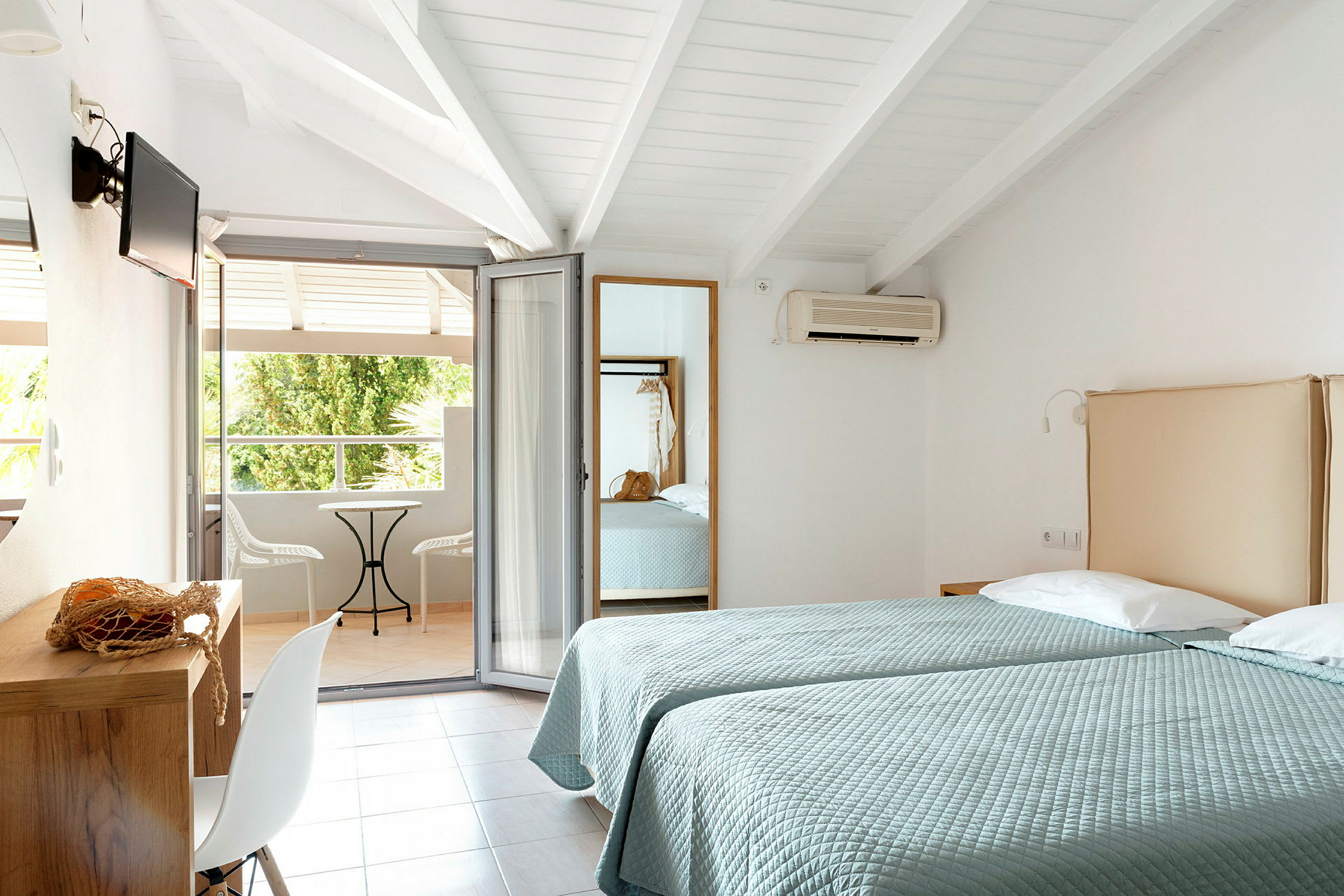 Två enkelsängar i ett hotellrum med öppning mot en möblerad balkong. (AI-genererad text)