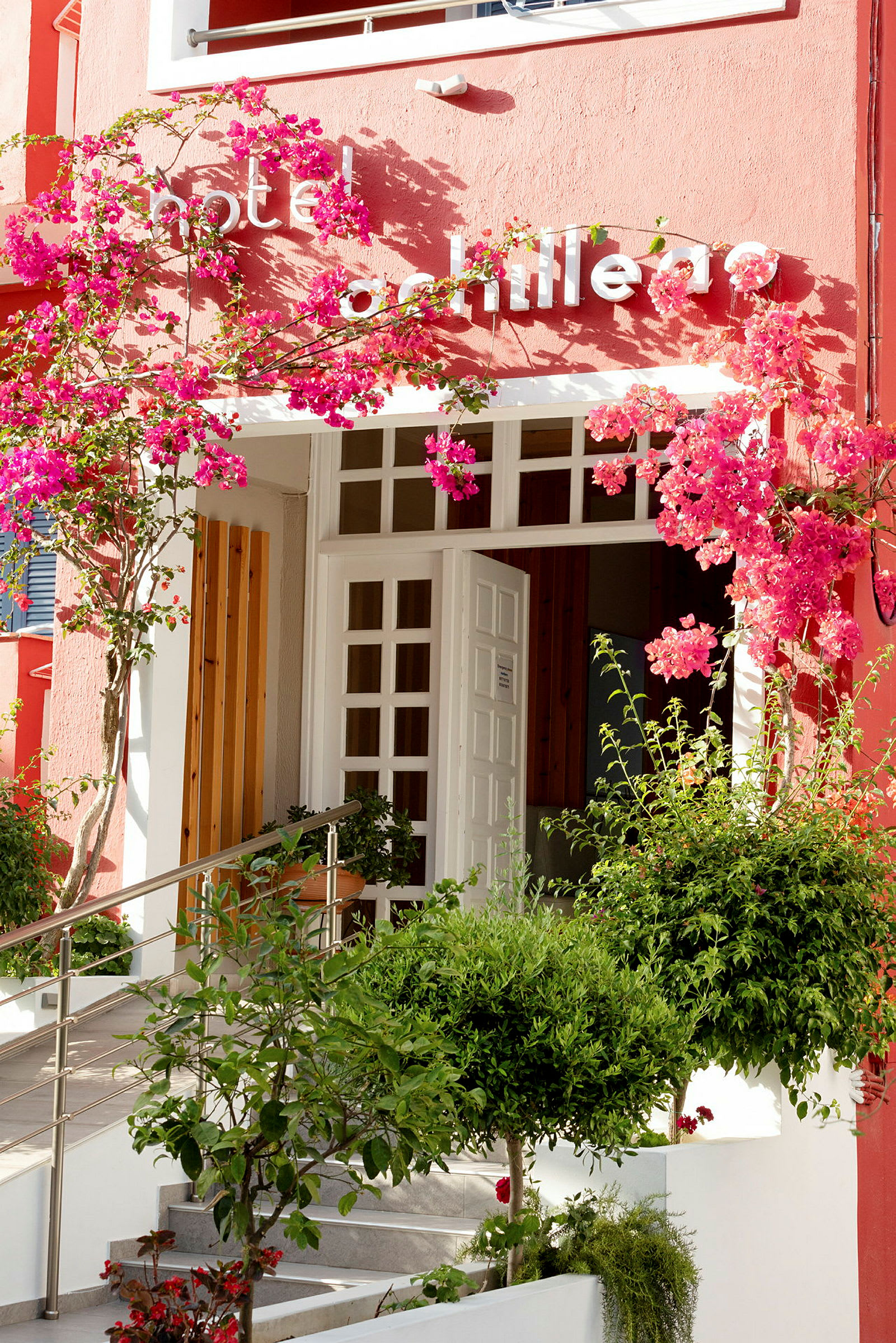 Ingång till hotell med vita dörrar och rosa blommor. (AI-genererad text)