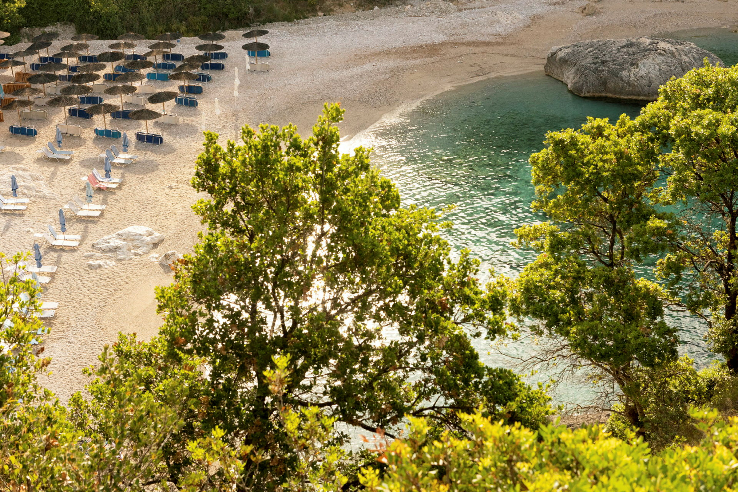 Strand med parasoller, solsängar, grönska och klart blått vatten. (AI-genererad text)