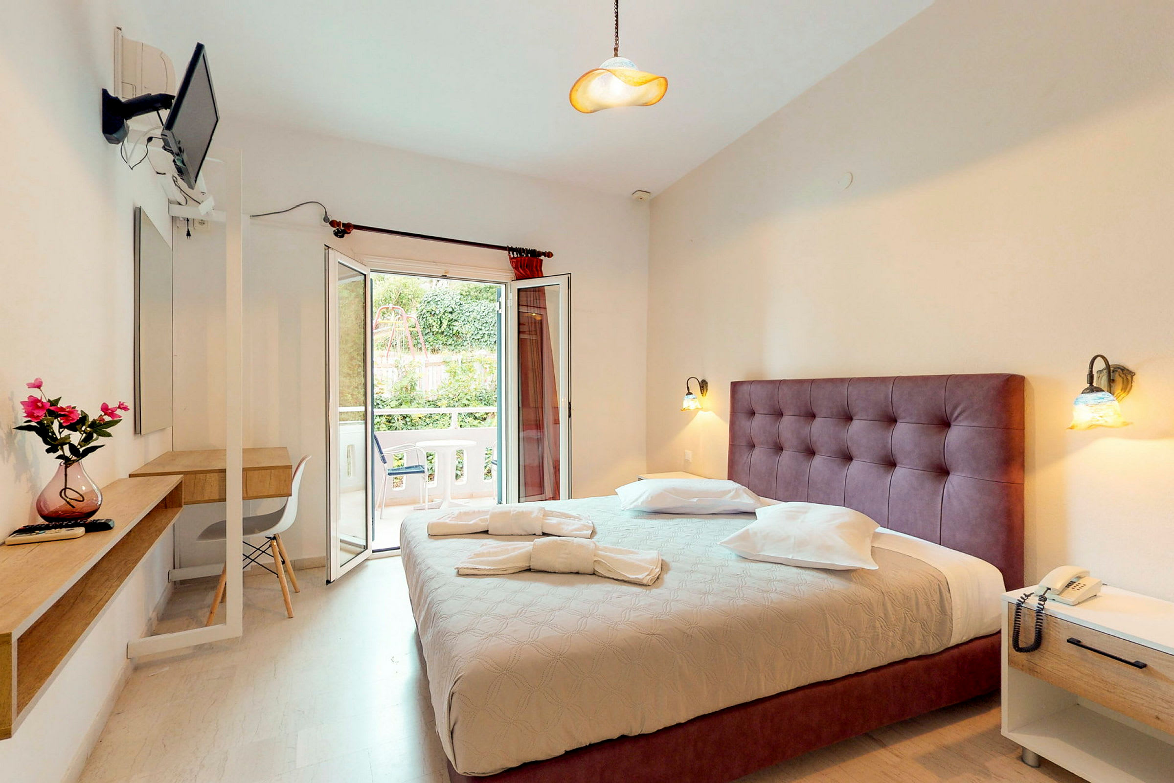 Ett hotellrum med en dubbelsäng, skrivbord och öppen balkongdörr. (AI-genererad text)