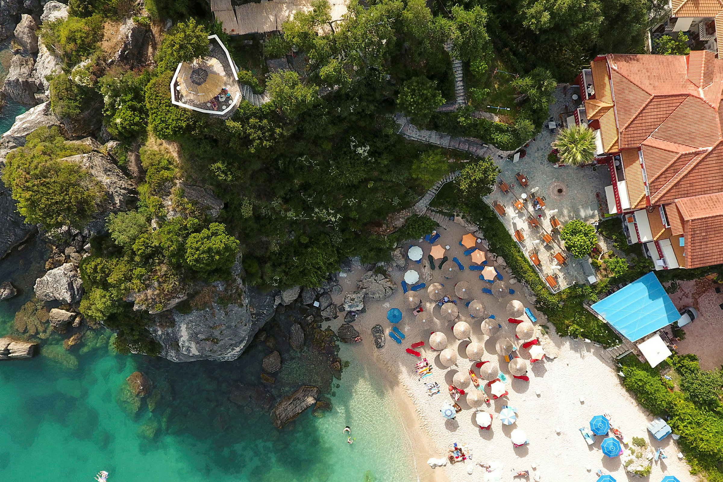 Flygfoto över en strand med parasoller, solsängar och omgivande gröna klippor. (AI-genererad text)