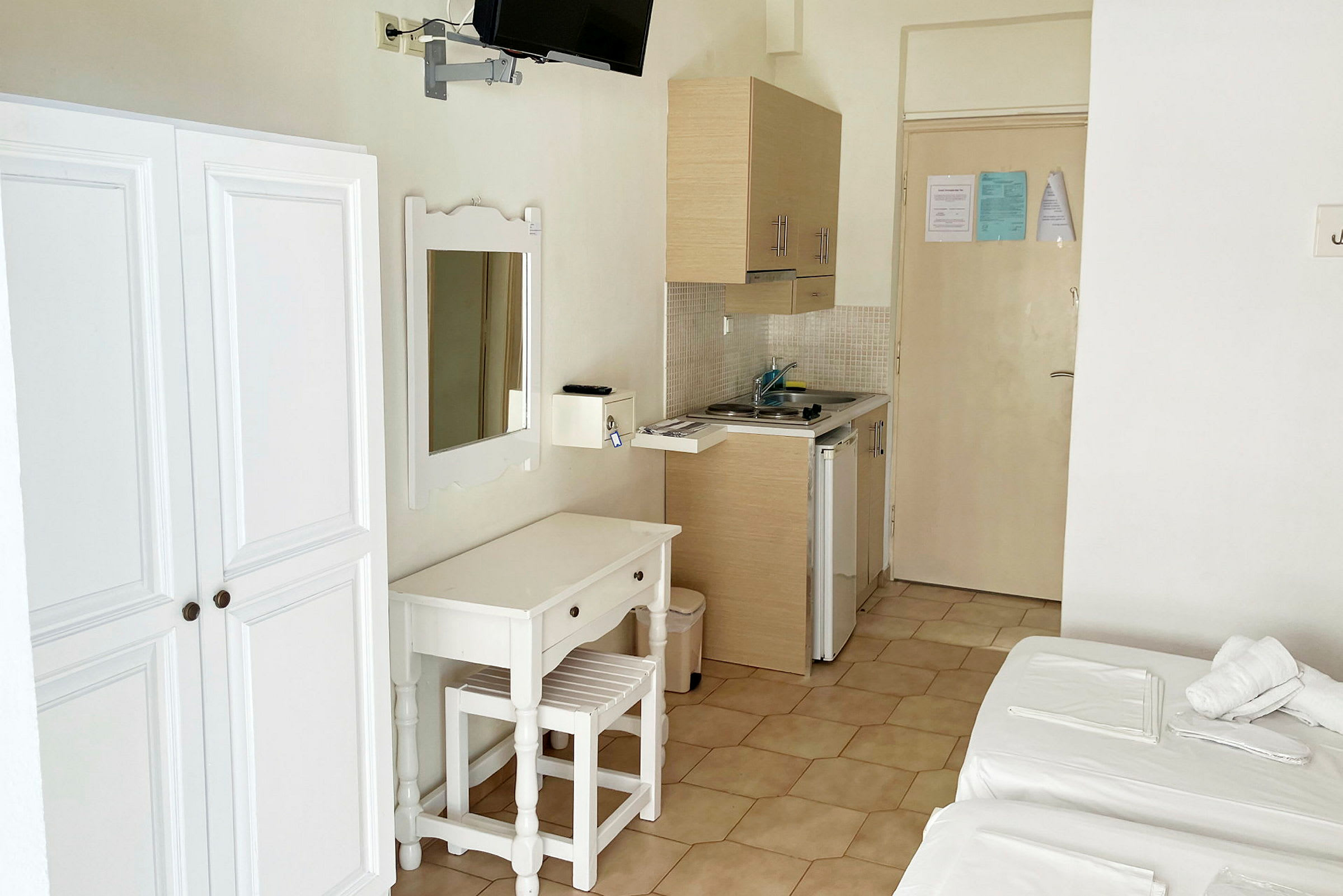 Bild av ett hotellrum med en garderob, en spegel, en skrivbordsmöbel med stol och en liten köksdel med diskhon. (AI-genererad text)