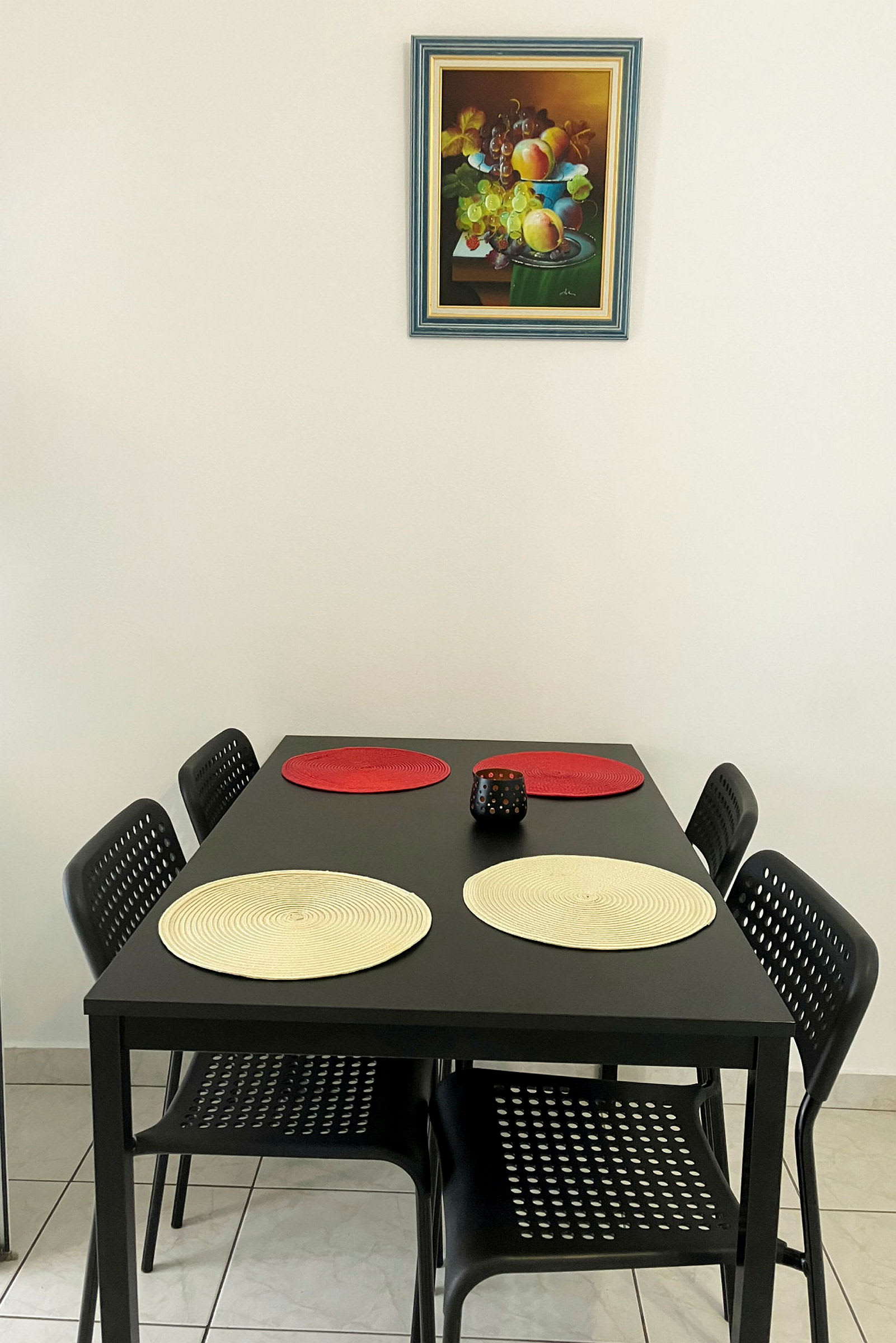 Ett matbord med fyra stolar, bordsmattor och en dekorativ ljushållare. (AI-genererad text)