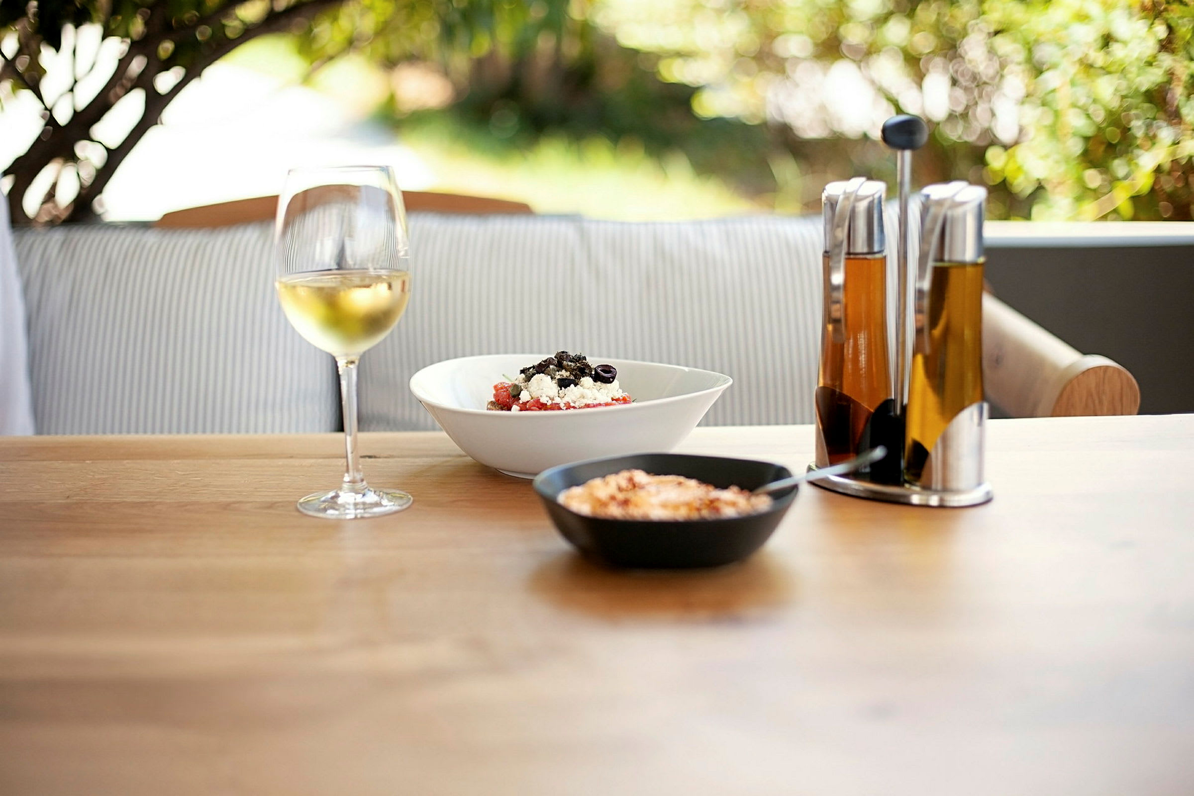 Ett dukat bord med ett glas vin, sallad, och oljeflaskor. (AI-genererad text)