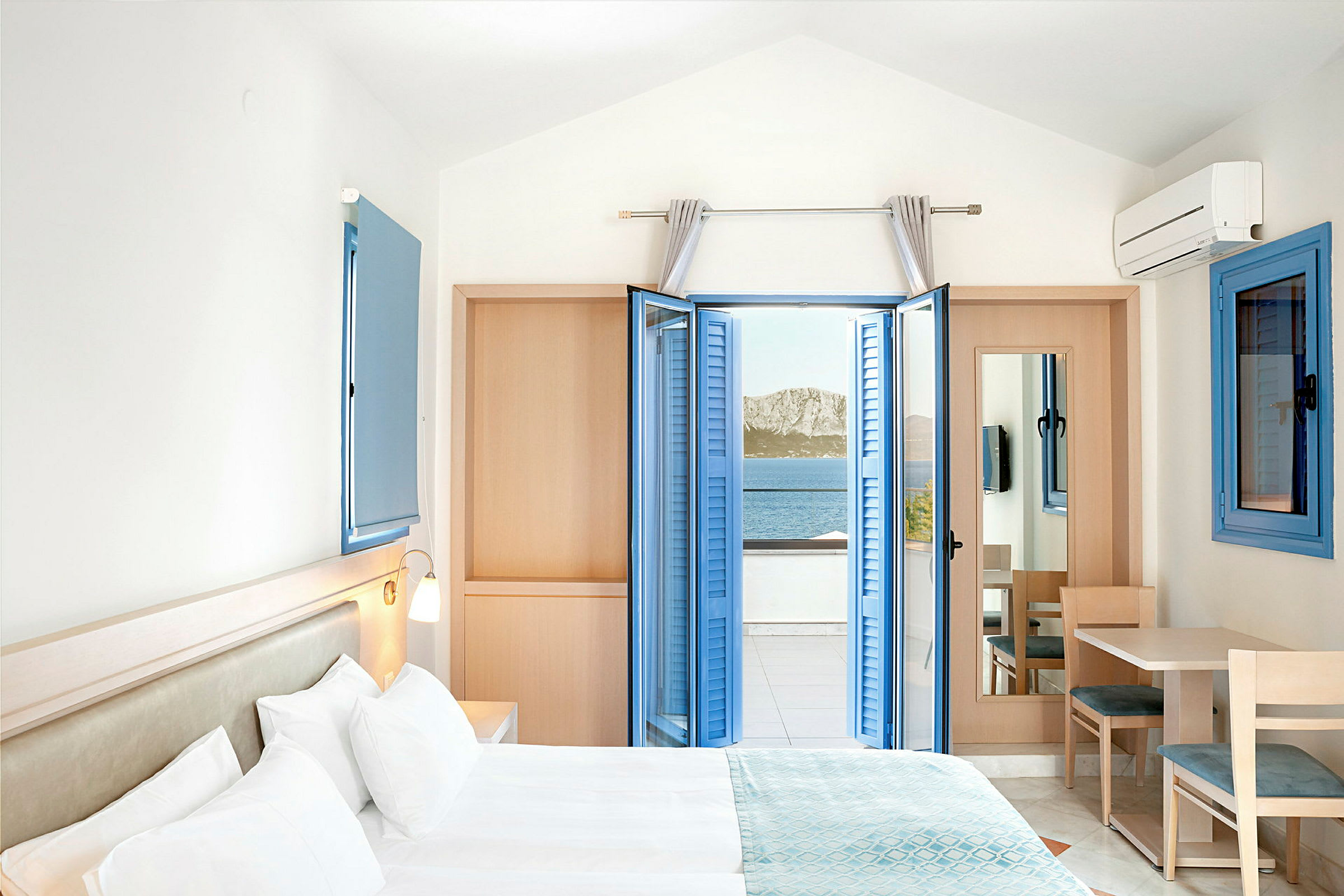 Hotellrum med dubbelsäng och havsutsikt genom öppna blå fönsterluckor. (AI-genererad text)