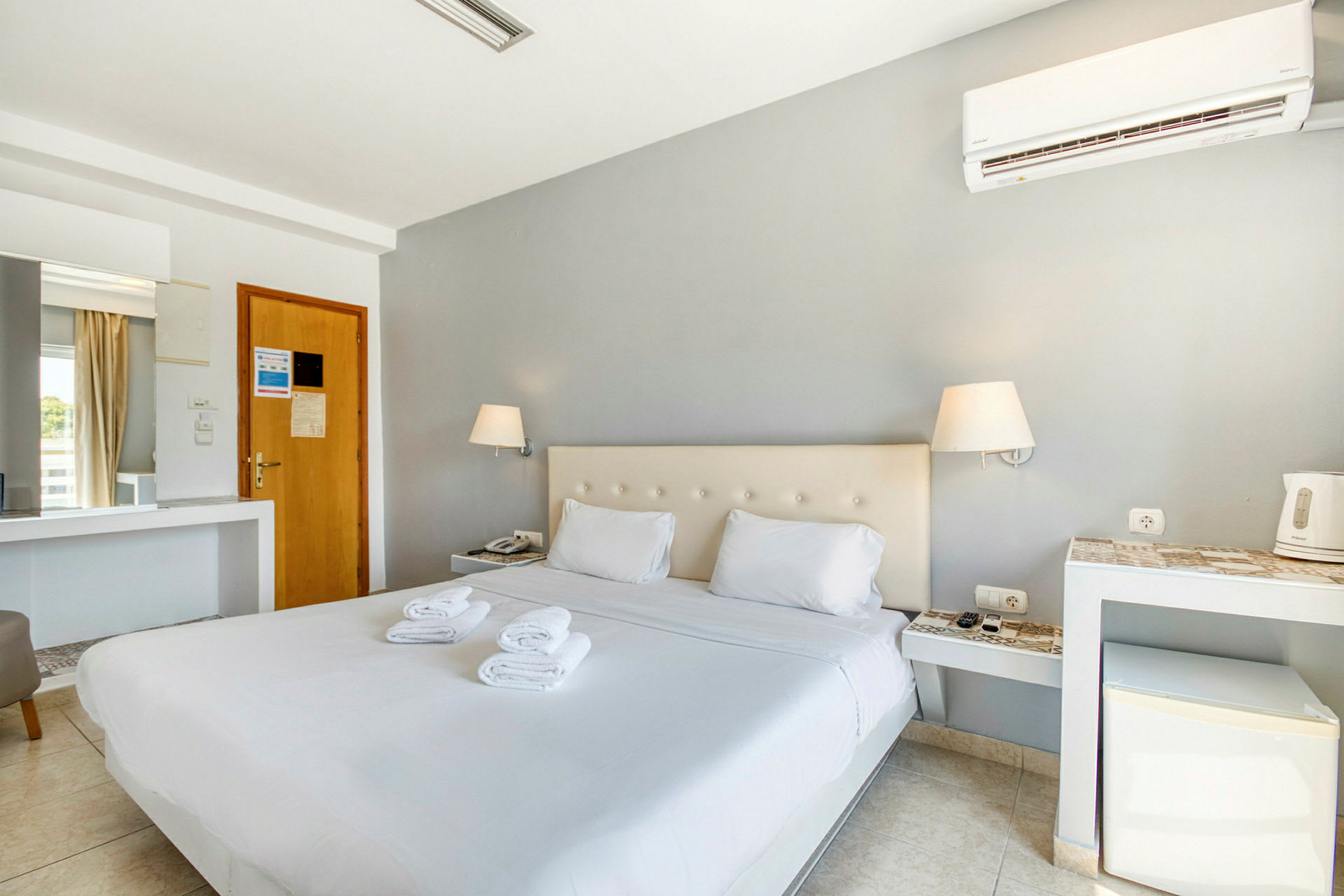 Ett hotellrum med en dubbelsäng, två lampor och en liten minikyl. (AI-genererad text)