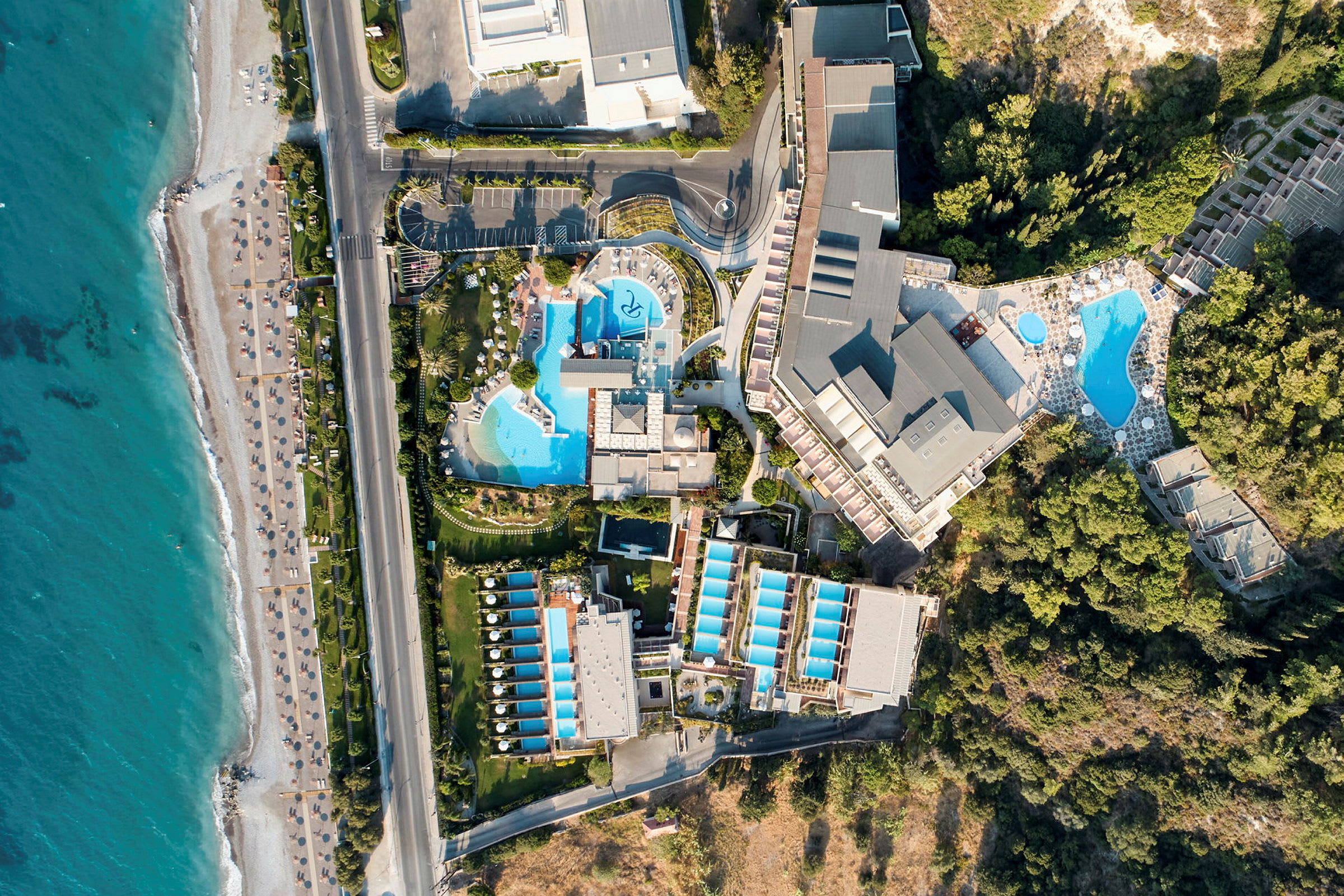 Flygbild av ett hotellområde med pooler, byggnader och närhet till stranden. (AI-genererad text)