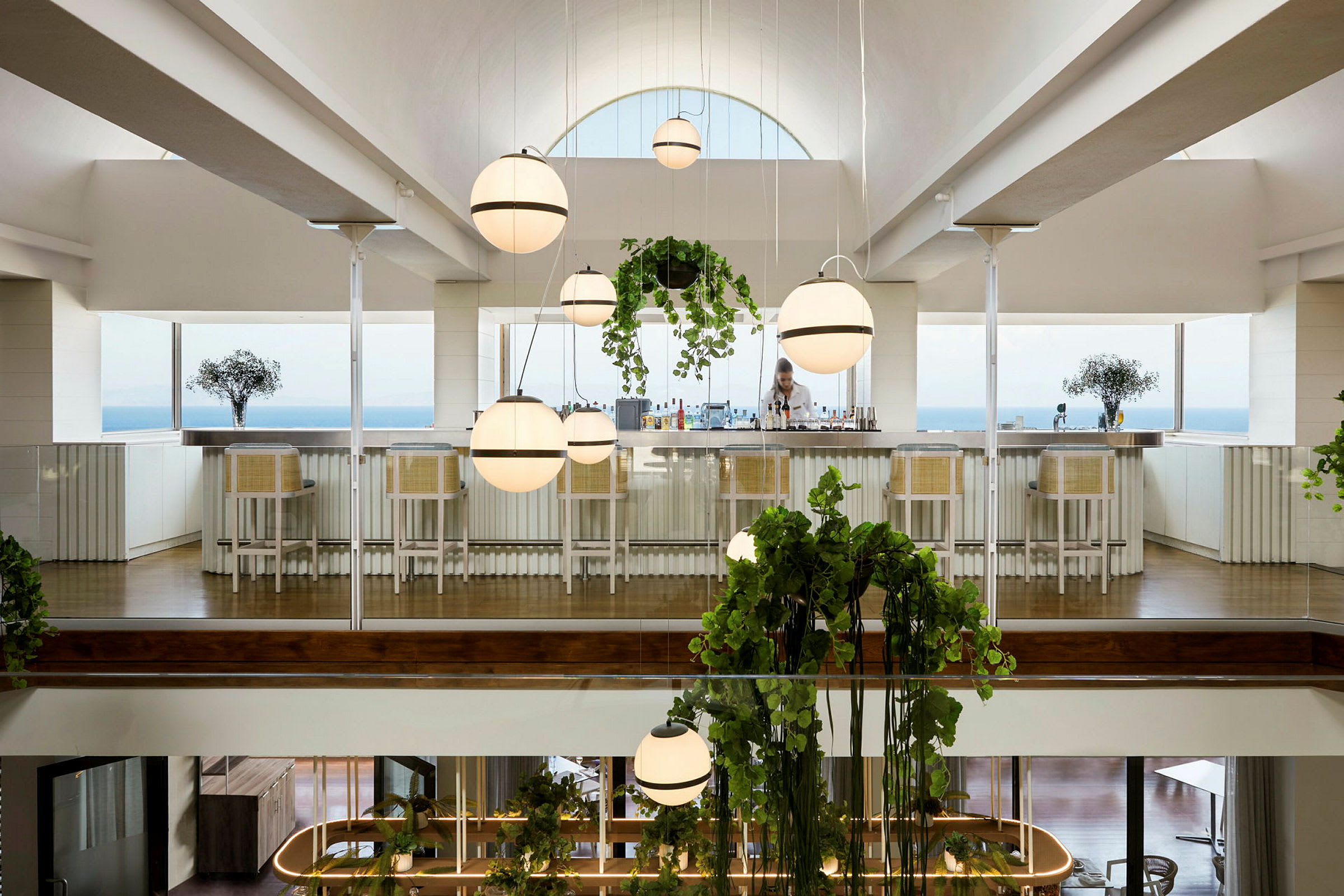 En upplyst bar med vita barstolar och hängande lampor, utsikt mot havet. (AI-genererad text)