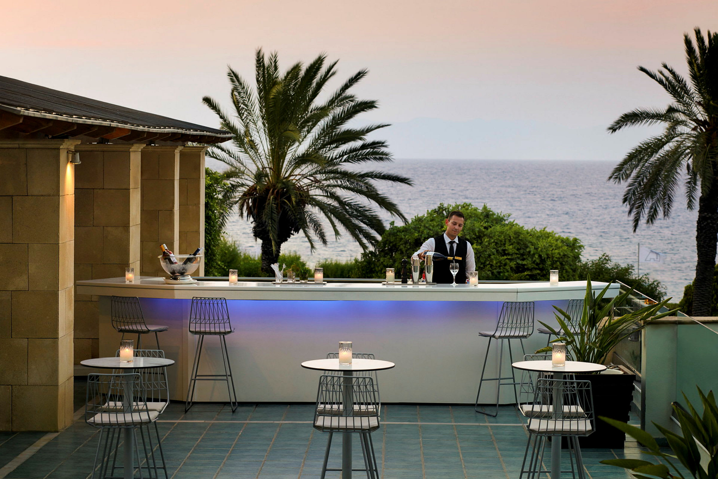 Uteserveringsområde med bar nära havet och omgivande grönska. (AI-genererad text)