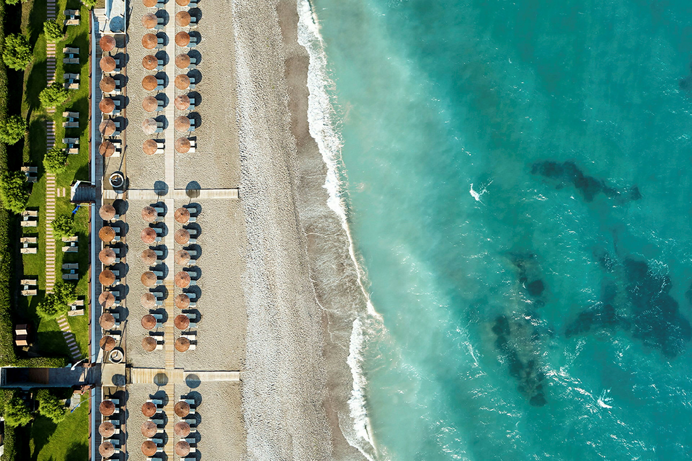 Flygfoto av en strand med parasoller och solsängar bredvid en turkosblå havsstrand. (AI-genererad text)