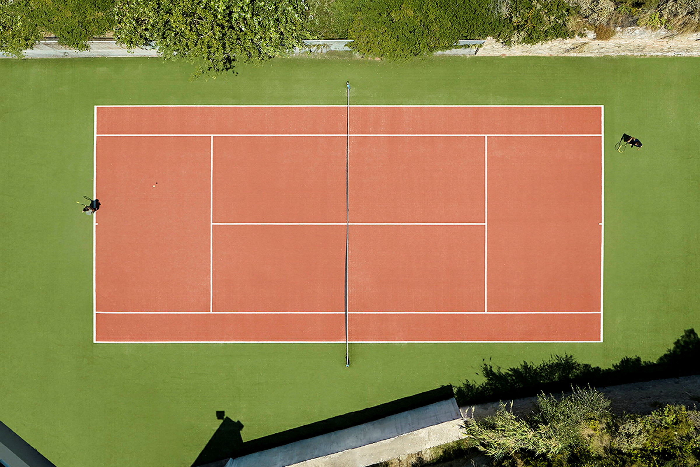 En tennisplan sedd ovanifrån med grön omgivning. (AI-genererad text)