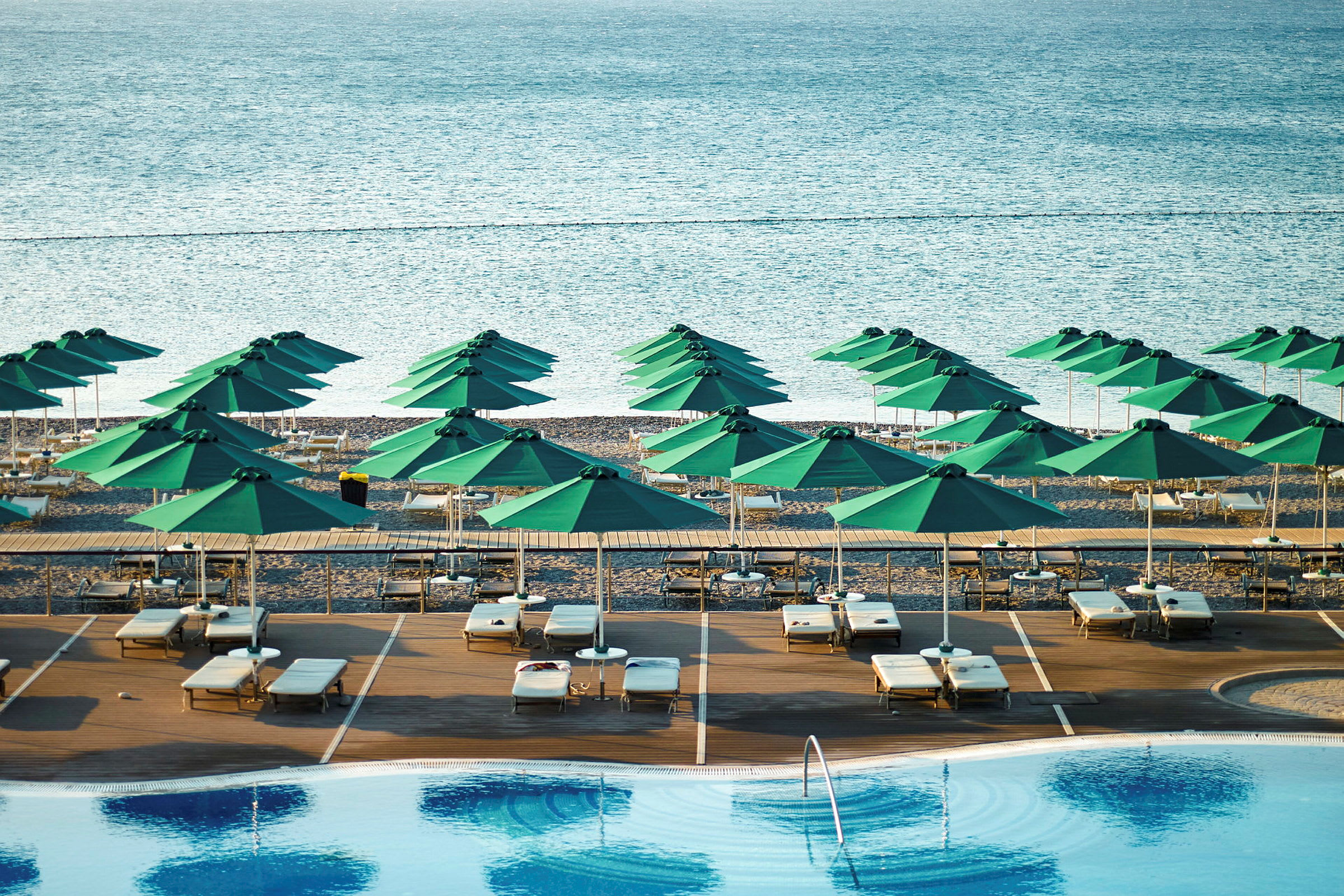 Strand med gröna parasoller och solstolar nära en pool. (AI-genererad text)
