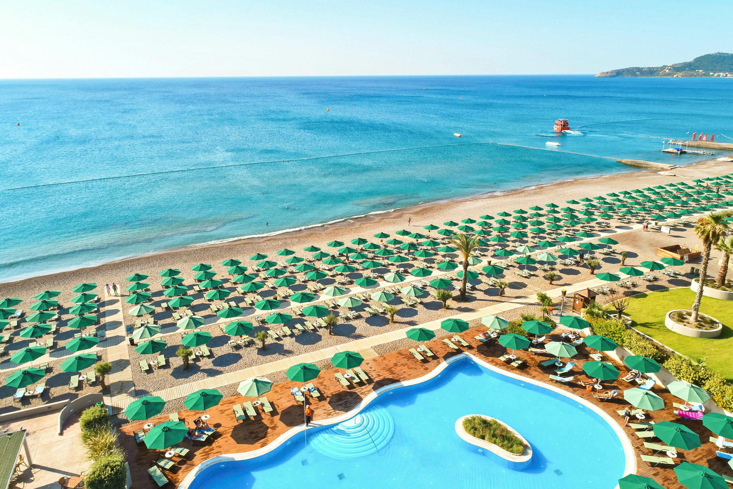 Vy över strand med solstolar och gröna parasoller. Framför stranden syns en pool. (AI-genererad text)