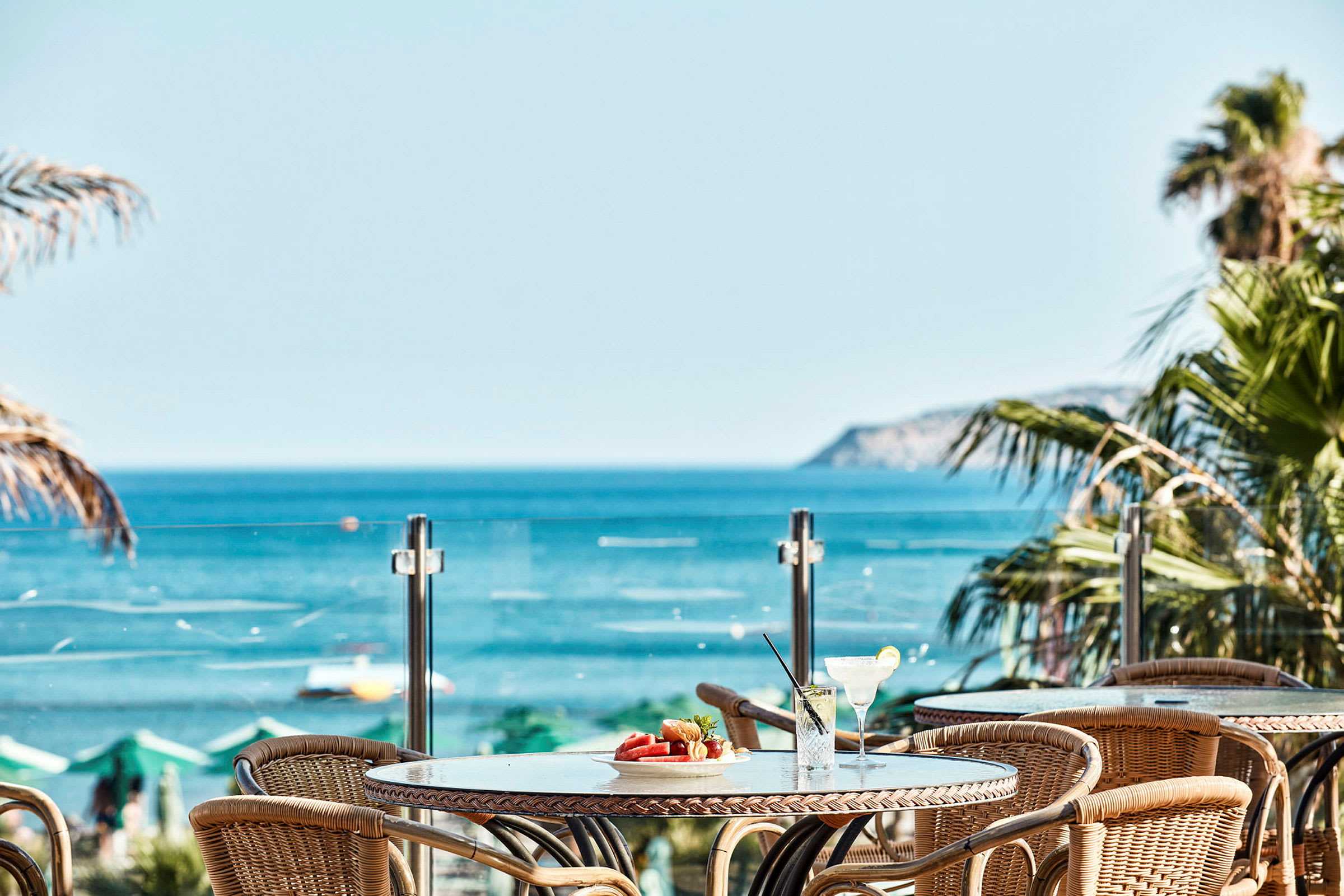 Utsikt över bord med drinkar och frukt mot havet. (AI-genererad text)