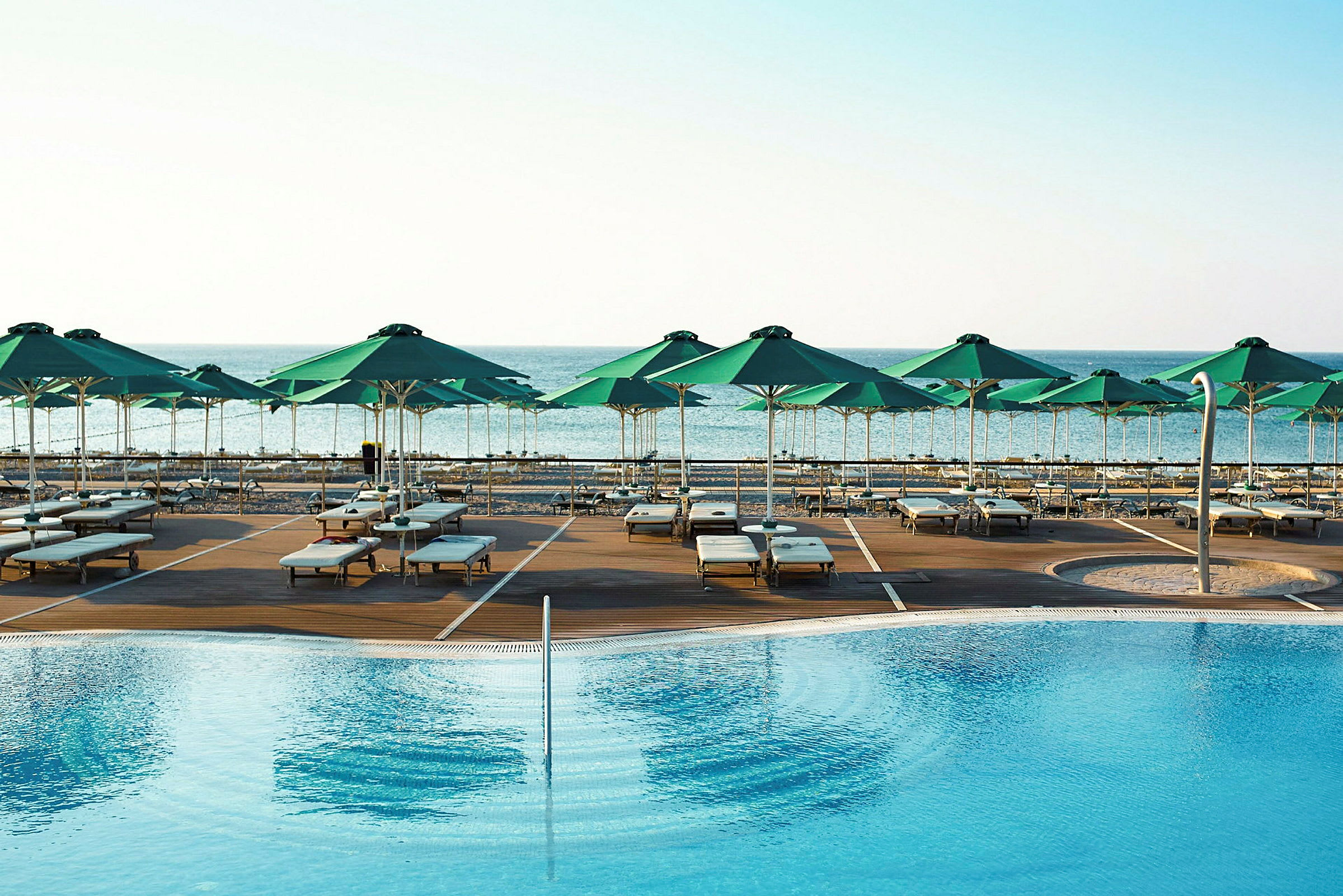 En pool med solstolar och gröna parasoller vid havet. (AI-genererad text)