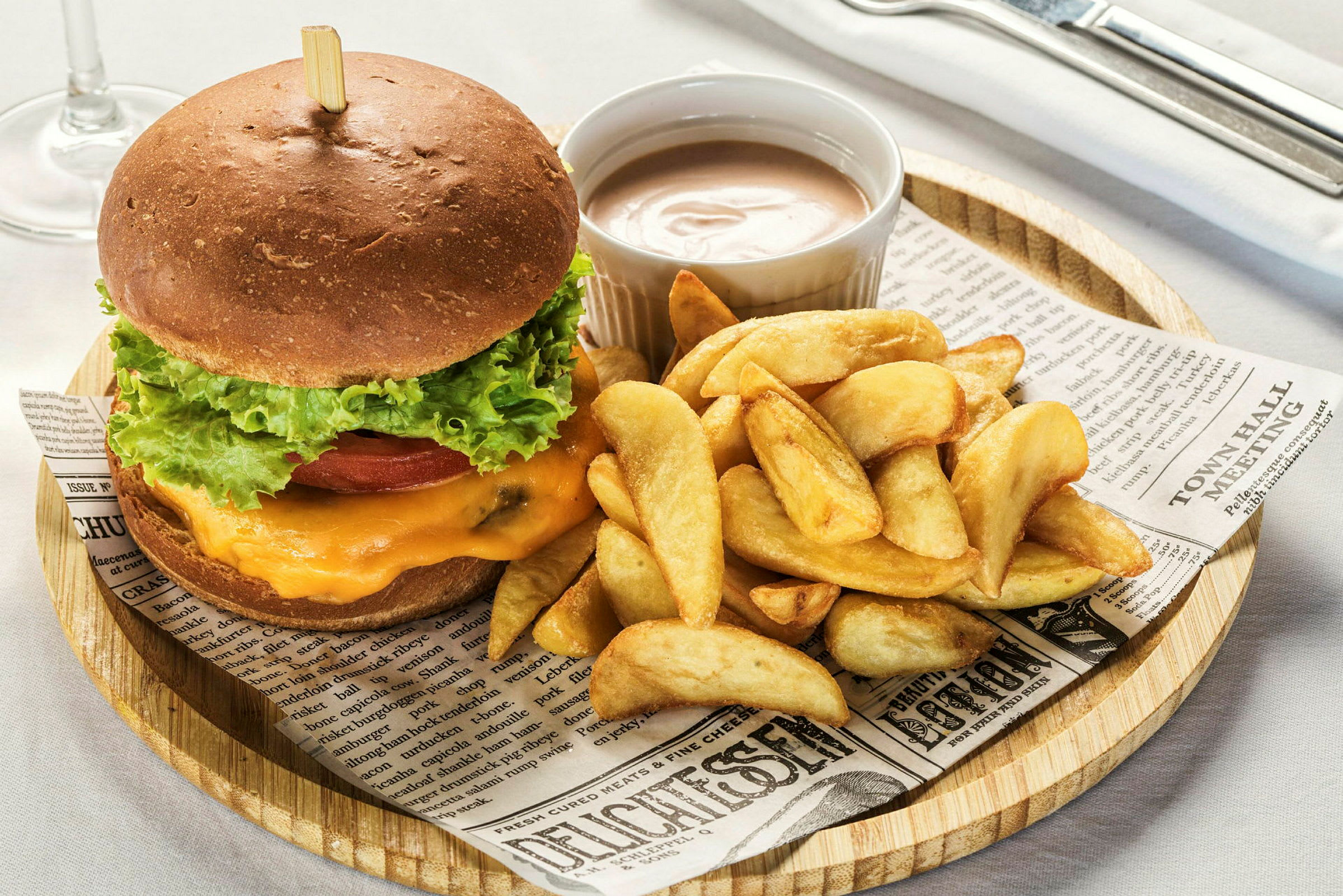 En hamburgare med sallad, tomat och ost serverad med klyftpotatis och en dipsås. (AI-genererad text)