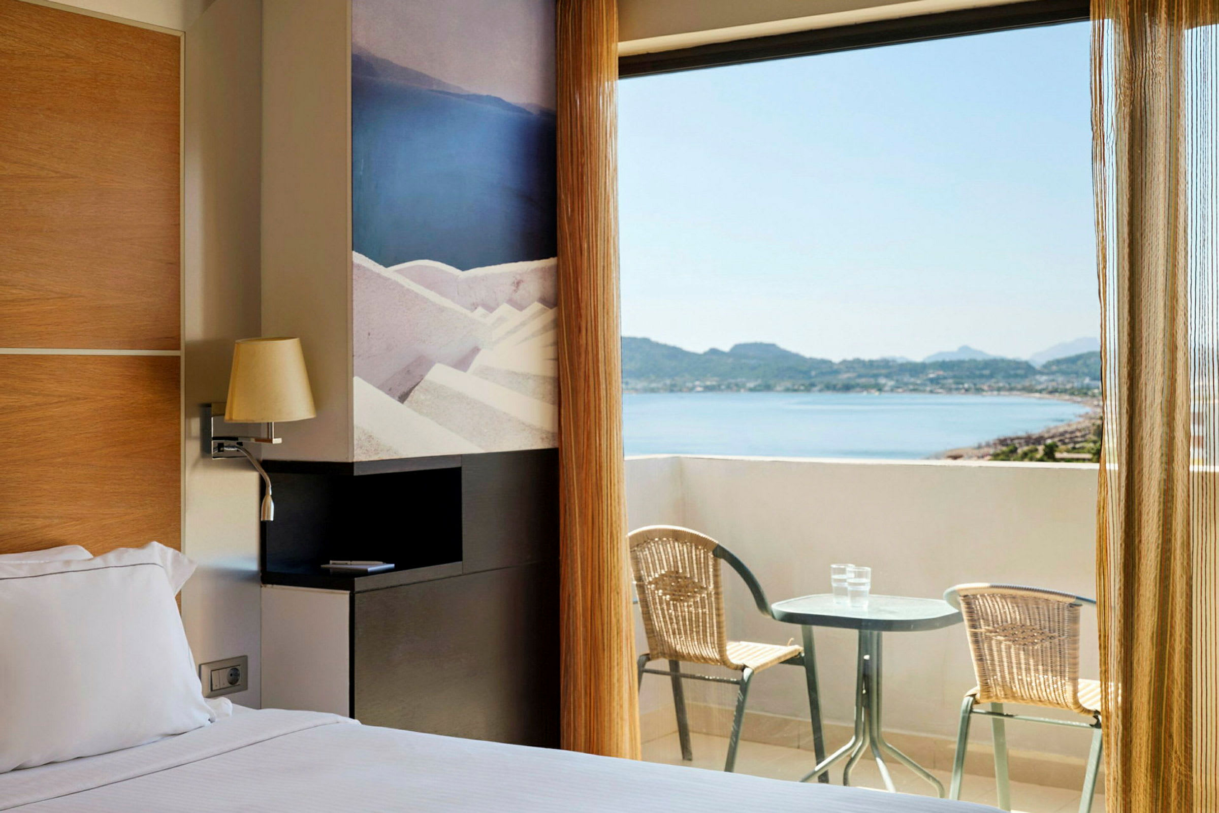 Hotellrum med dubbelsäng och utgång till en balkong med utsikt över havet. (AI-genererad text)