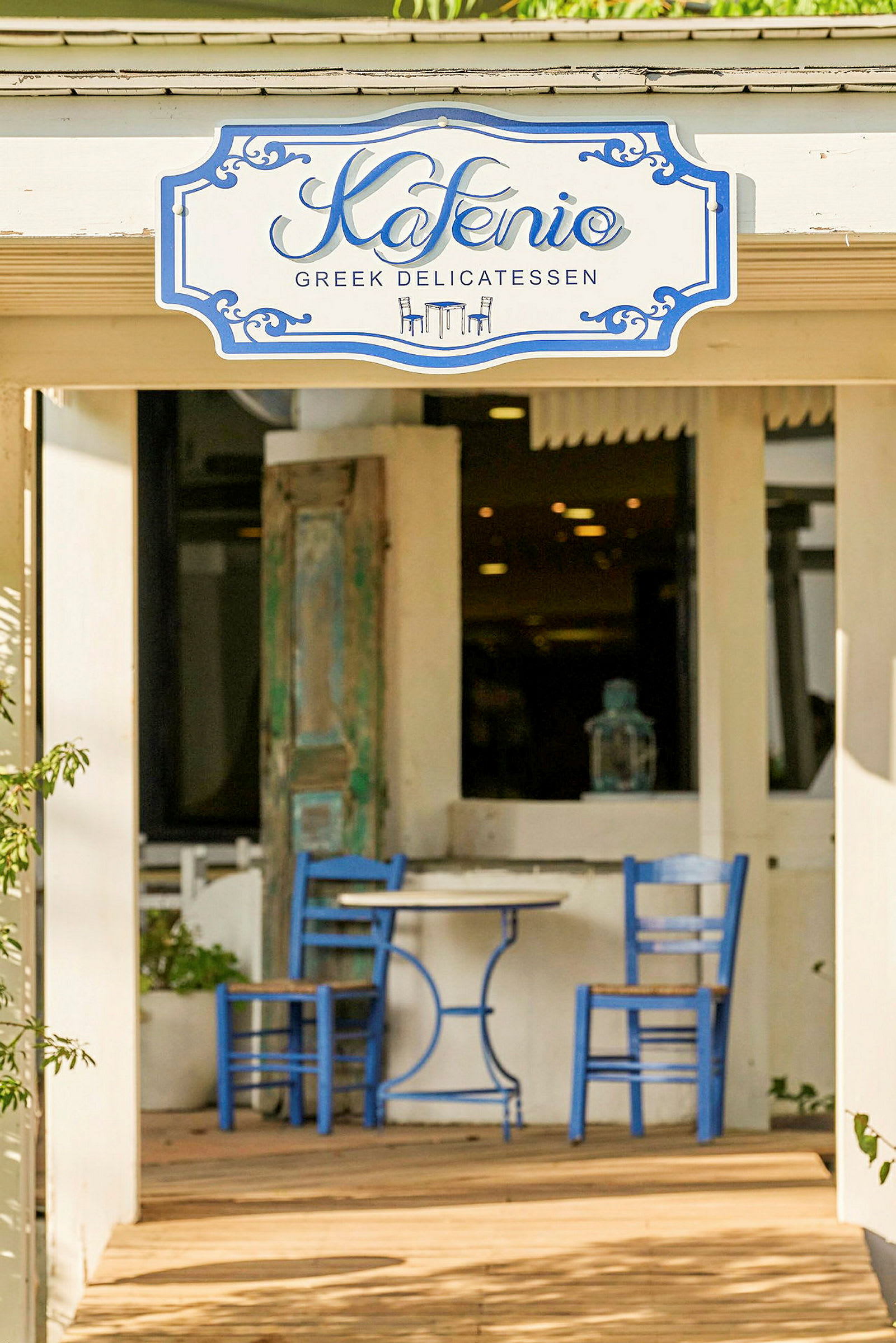 Ett café med ett skylt där det står 'Kafenio' och en uteplats med blå stolar och bord. (AI-genererad text)