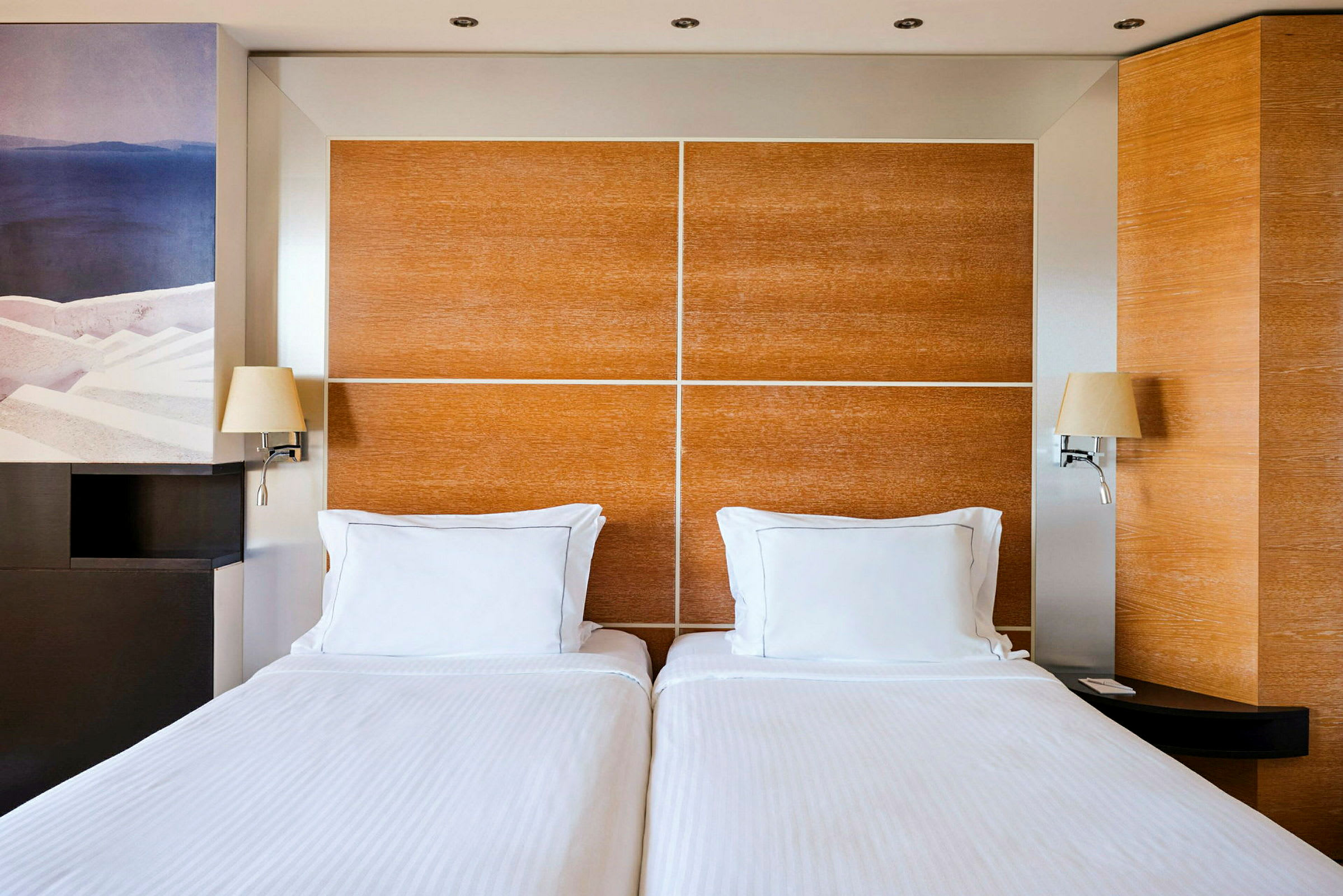Ett hotellrum med två enkelsängar med vita sängkläder och en träpanel som sänggavel. (AI-genererad text)