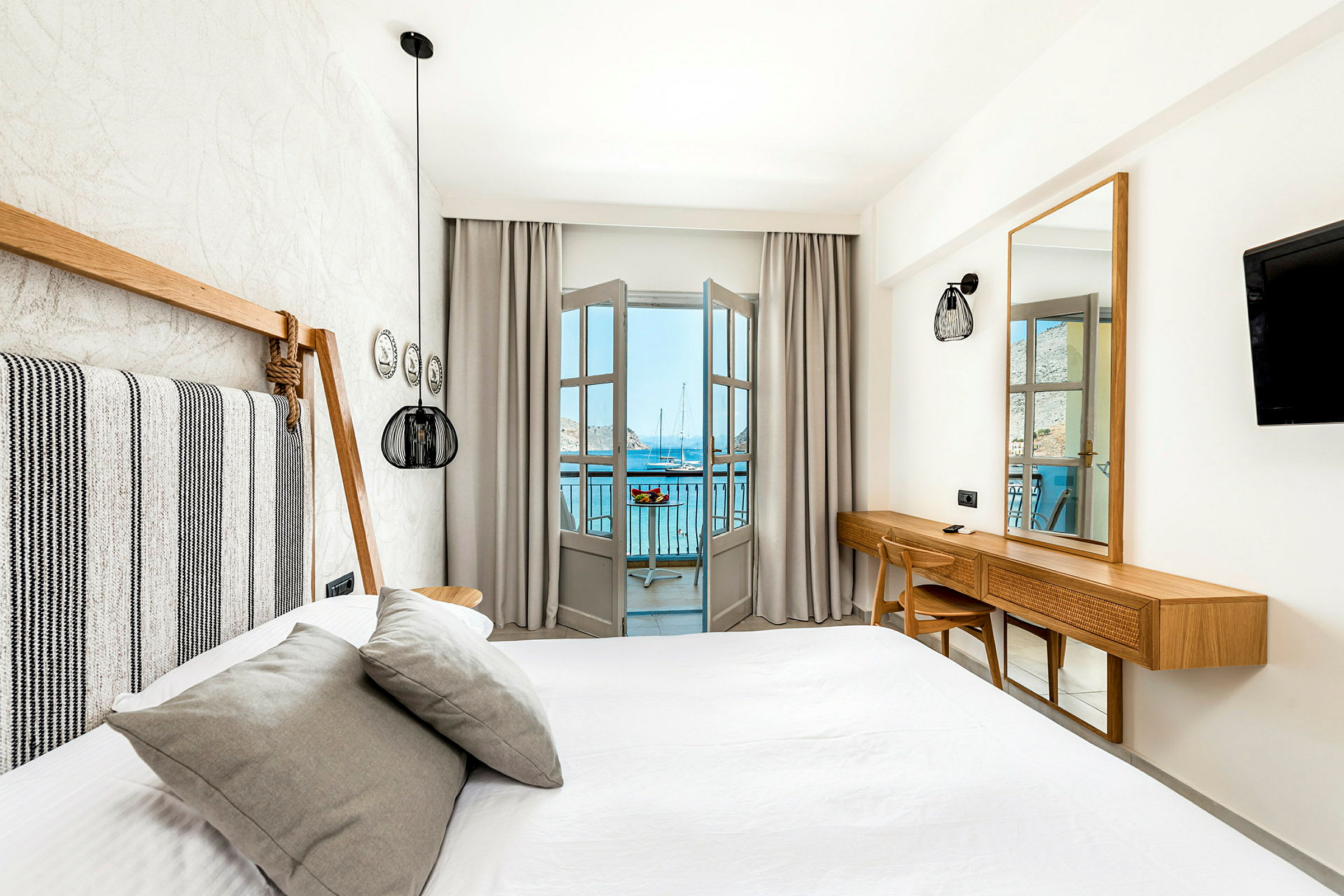 Ett ljust och modernt inrett hotellrum med säng och utsikt mot havet från en balkong. (AI-genererad text)