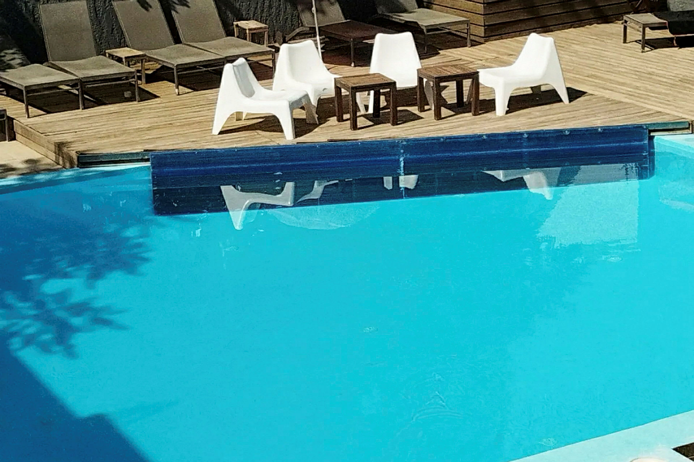 Trädäck vid en pool med flera solstolar och en sittgrupp. (AI-genererad text)