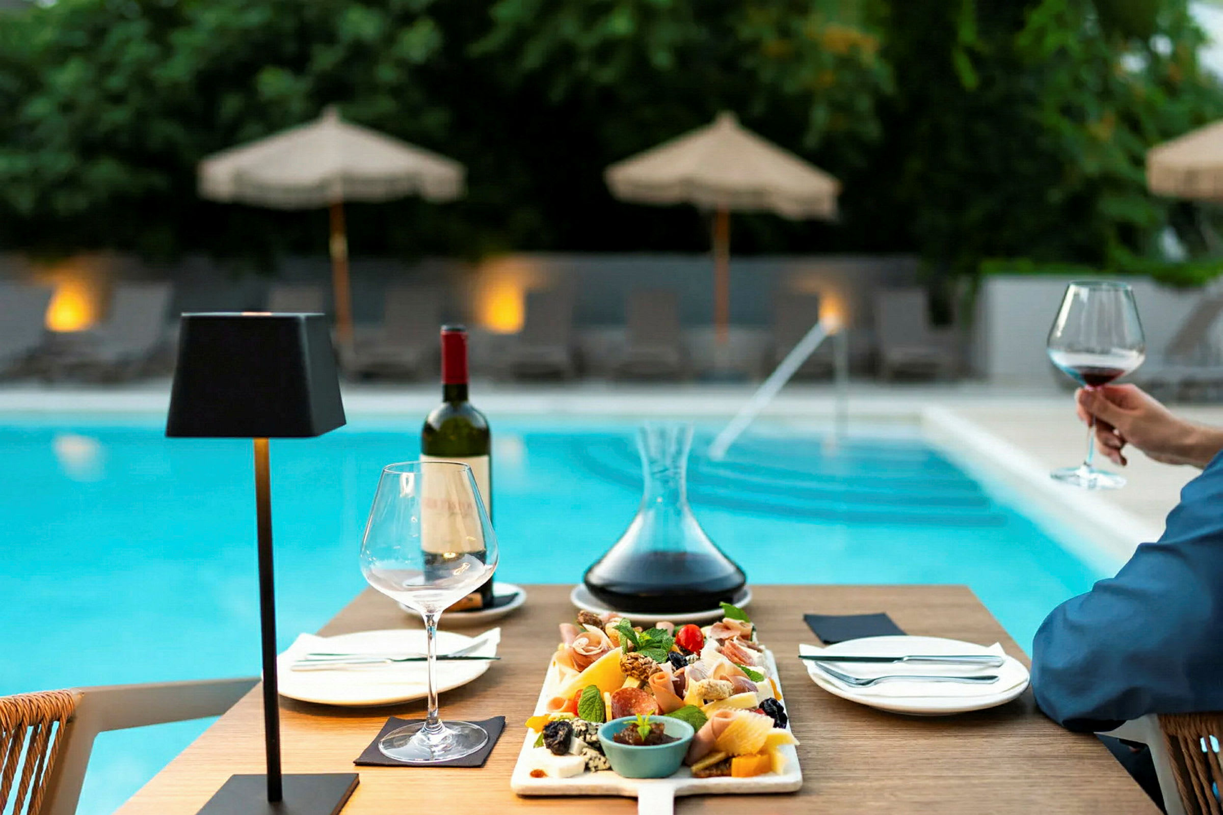 En tallrik med tilltugg och en karaff vin på ett bord nära en pool. (AI-genererad text)