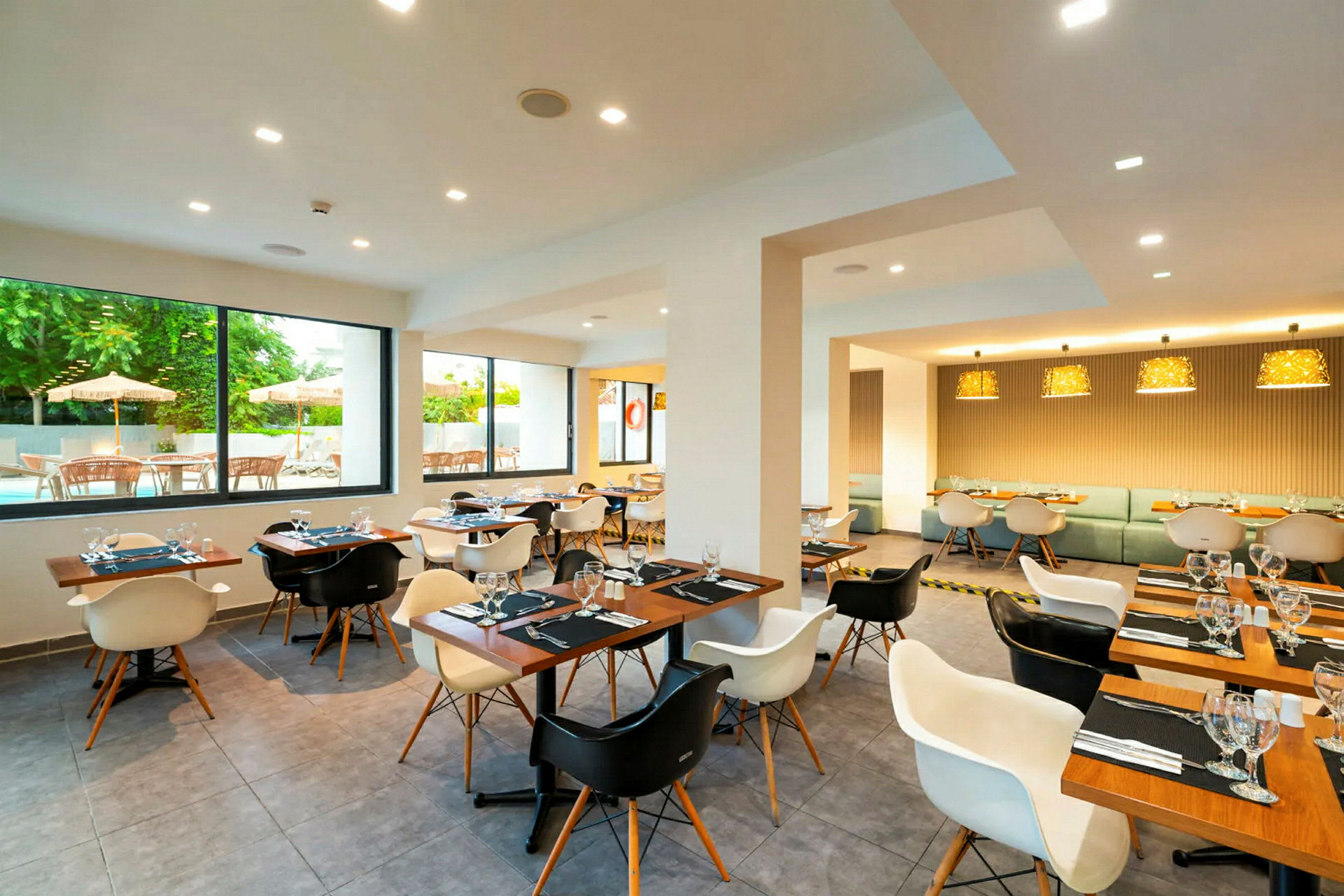 En modern restaurang med trämöbler, fönster med utsikt mot en uteservering och flera borddukningar. (AI-genererad text)